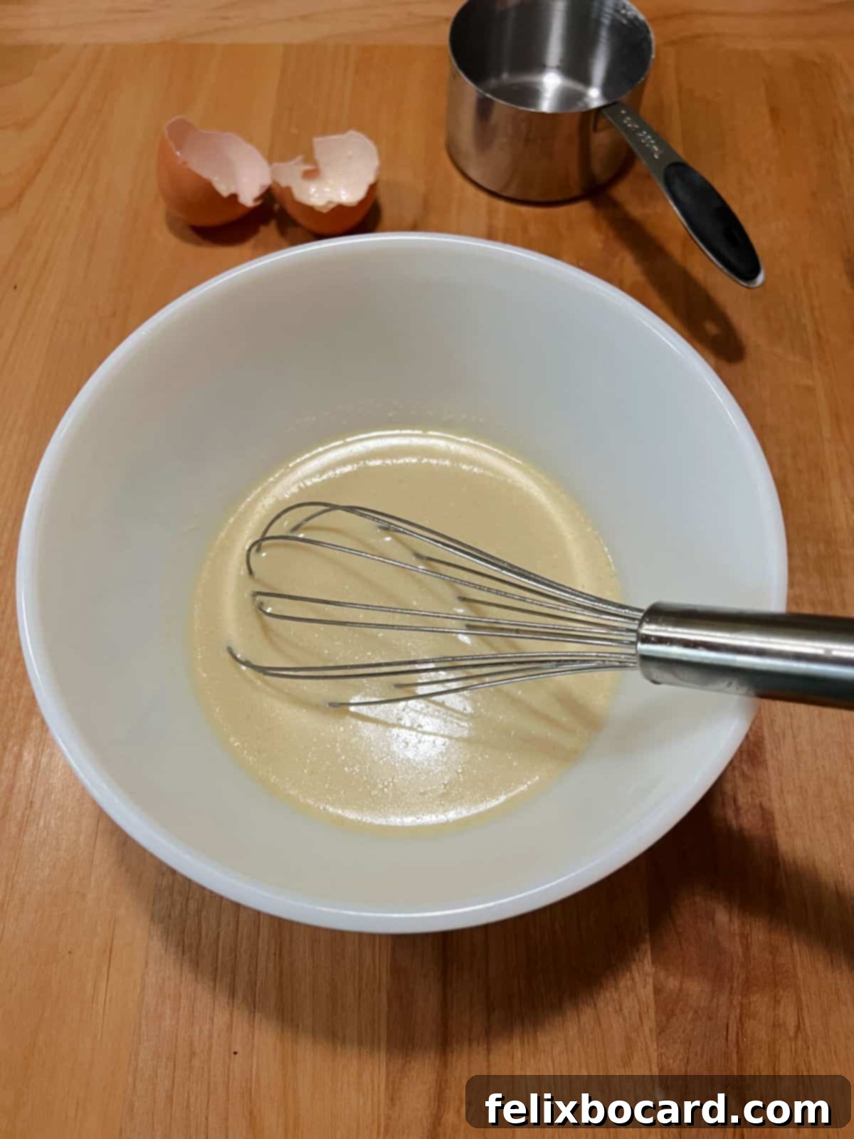A hand vigorously whisking a smooth, thin crepe batter in a mixing bowl.