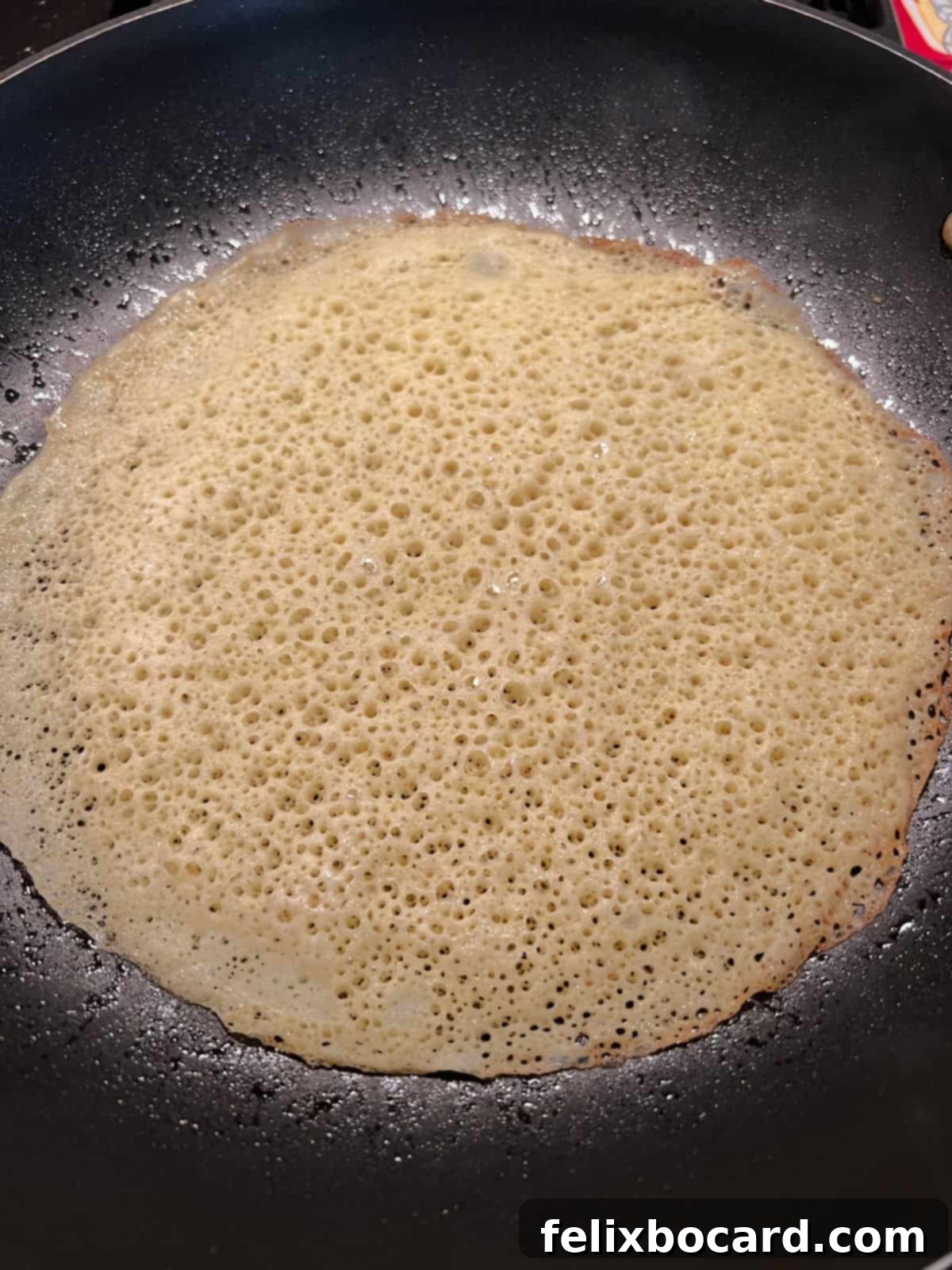 A thin crepe made with pancake mix beginning to cook in a non-stick skillet, showing the edges starting to crisp.