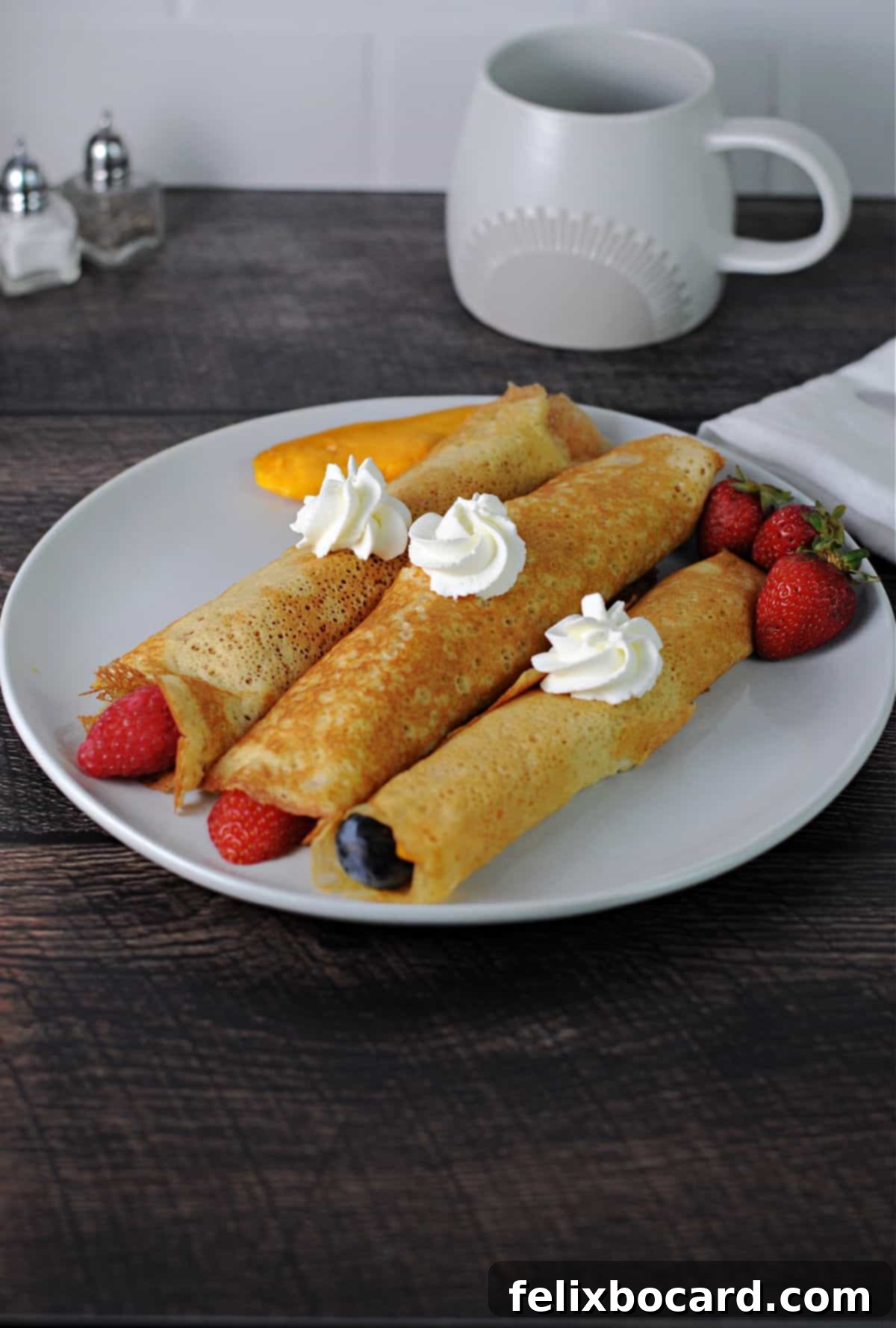 Three beautifully presented crepes from pancake mix, each rolled with fruit and topped with a generous dollop of whipped cream, ready to be enjoyed.