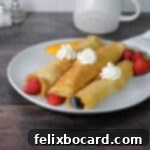 Three golden crepes made from pancake mix on a plate, rolled with fruit and topped with whipped cream, photographed from above.