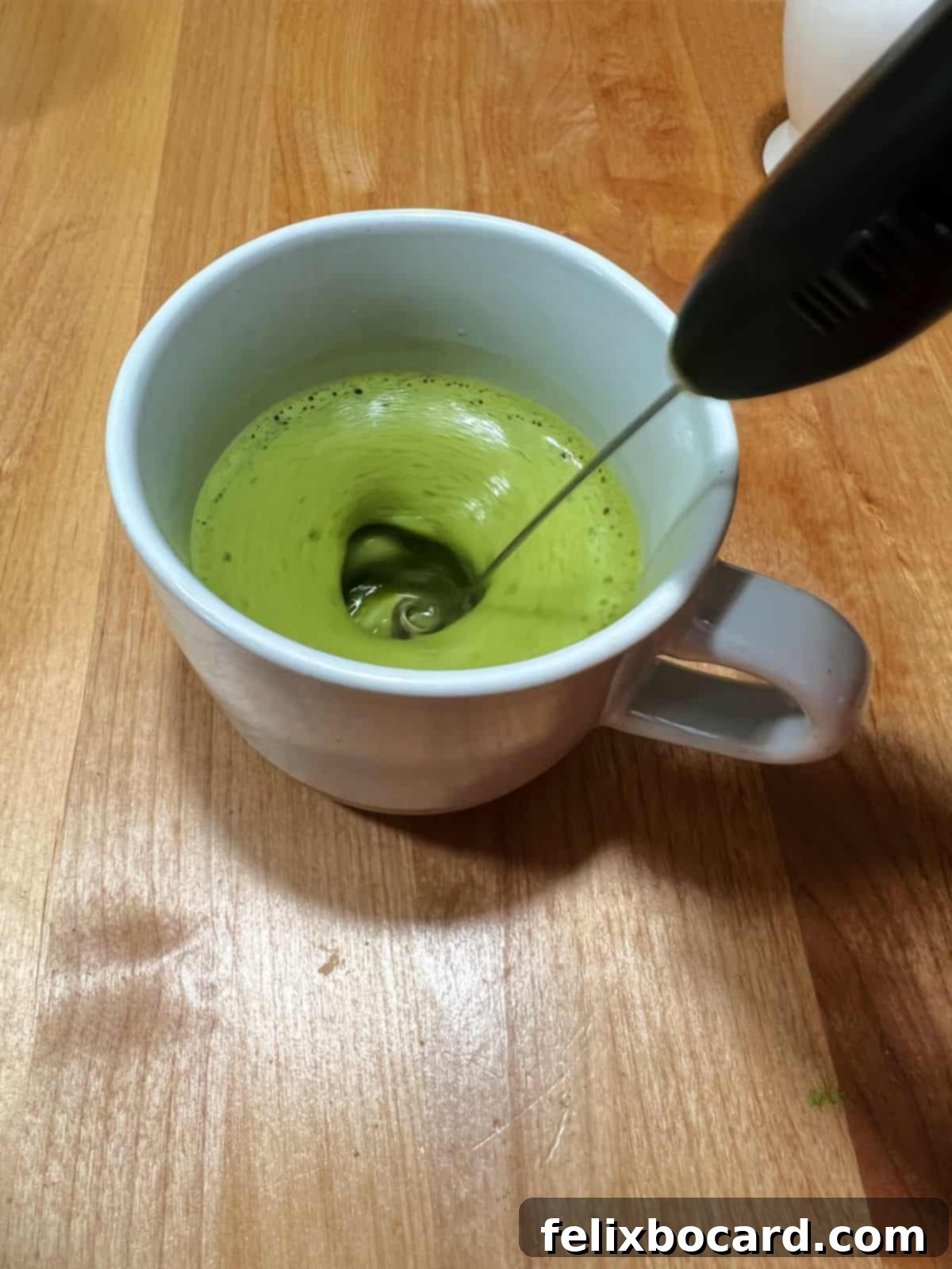 battery operated whisk mixing green matcha powder in water.