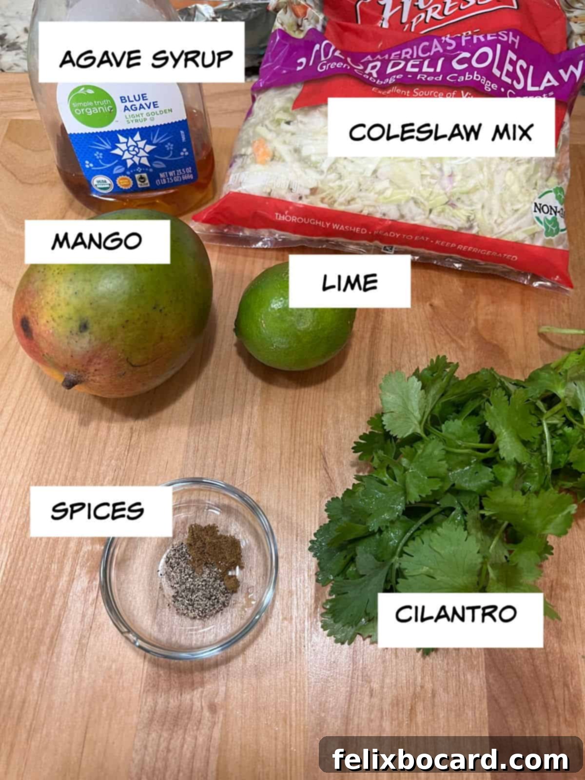 Tropical Mango Slaw for Fish Tacos 3 A flat lay image displaying all the simple, fresh ingredients for mango slaw: agave syrup in a small dish, a bag of coleslaw mix, a whole lime, fresh cilantro sprigs, a whole ripe mango, and small containers of spices.