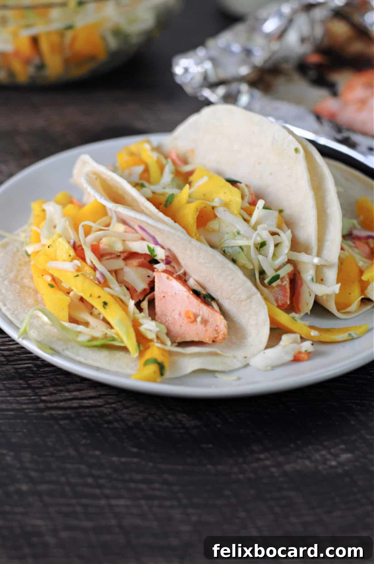 BBQ Salmon Tacos with Tangy Slaw 2 Three soft tortillas generously filled with flaky BBQ salmon and vibrant mango slaw, garnished with fresh cilantro.