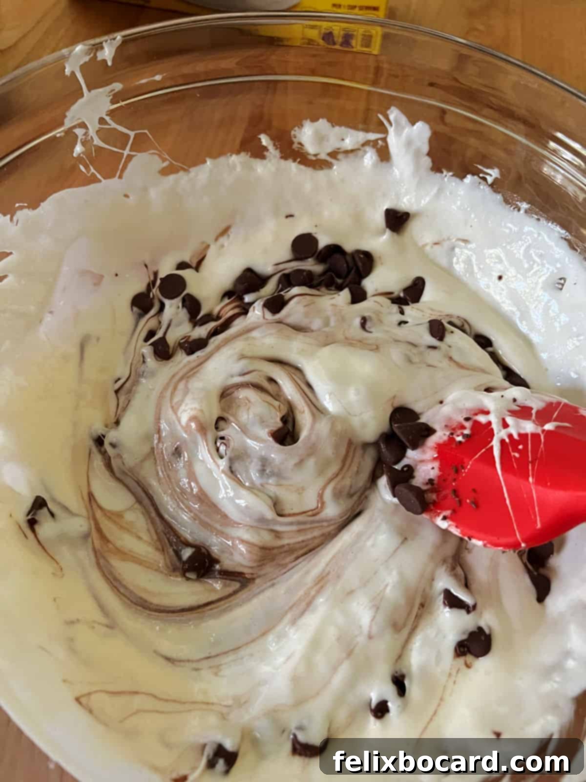 Adding milk chocolate chips to the warm, melted marshmallow and butter mixture.