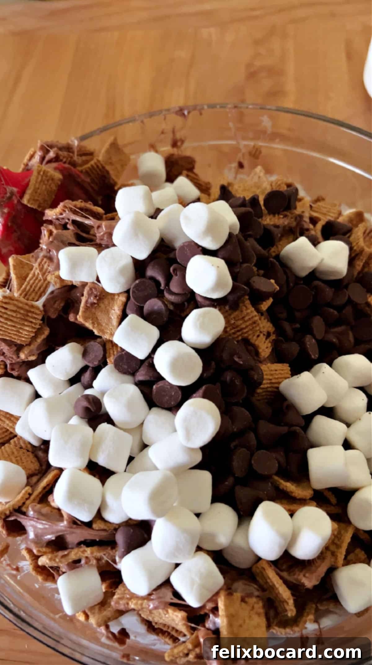 Chocolate chips and marshmallows sprinkled over the cereal mixture in a mixing bowl.