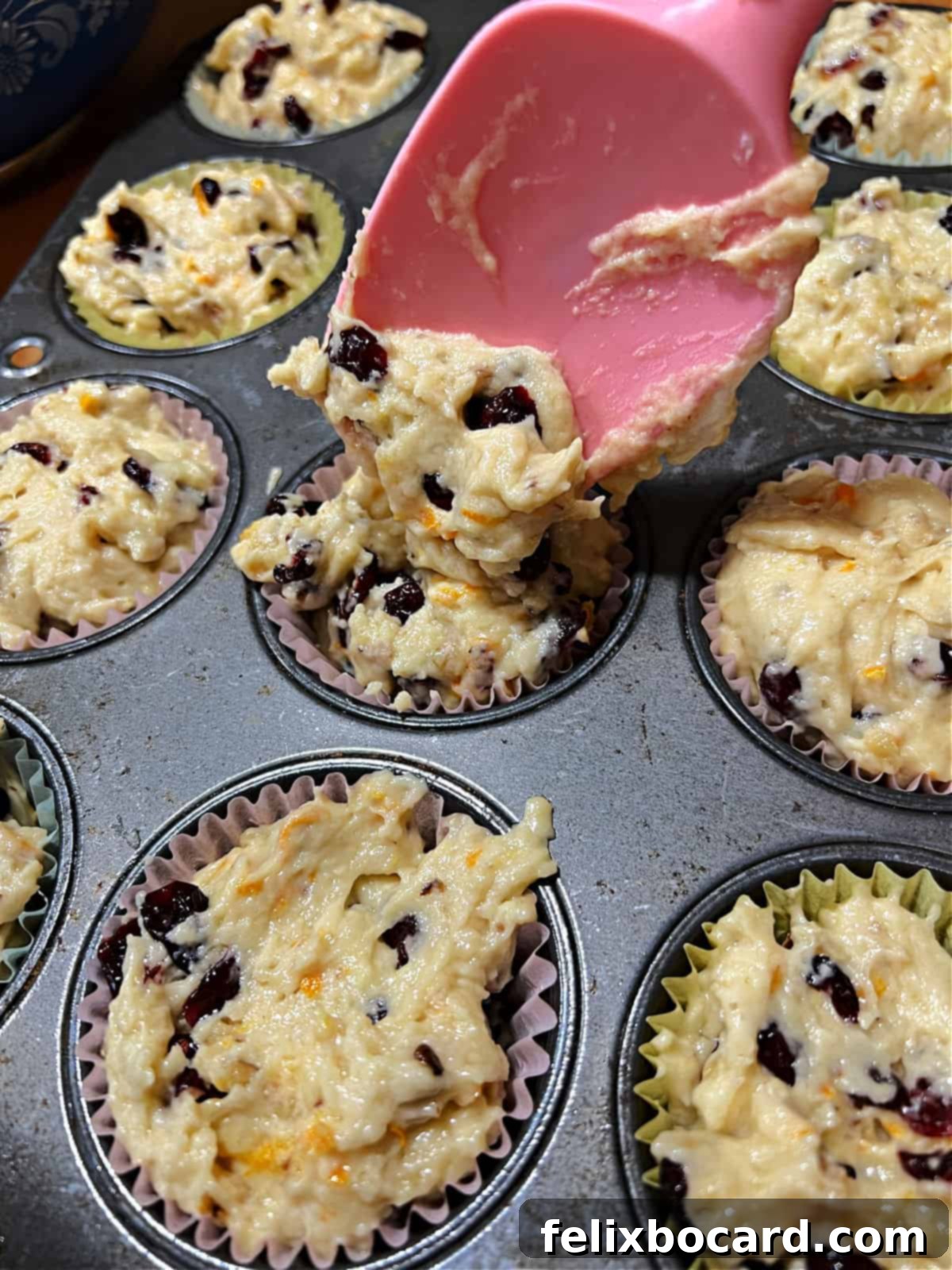 A spatula dropping muffin batter into paper-lined muffin cups.