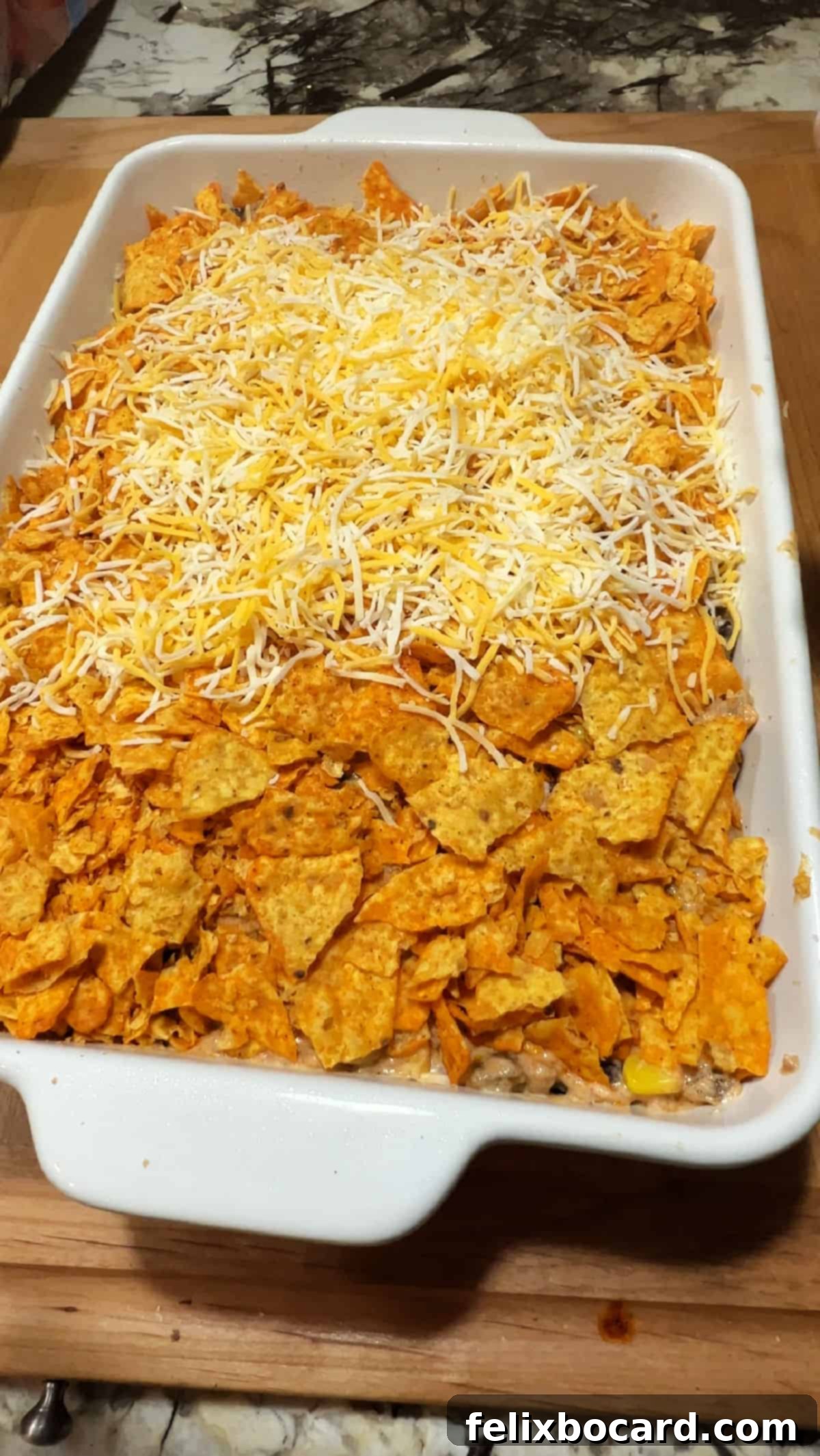 Cheesy Dorito Ground Beef Bake 6 Layers of Doritos, meat mixture, and cheese assembled in a baking pan, ready for the oven.