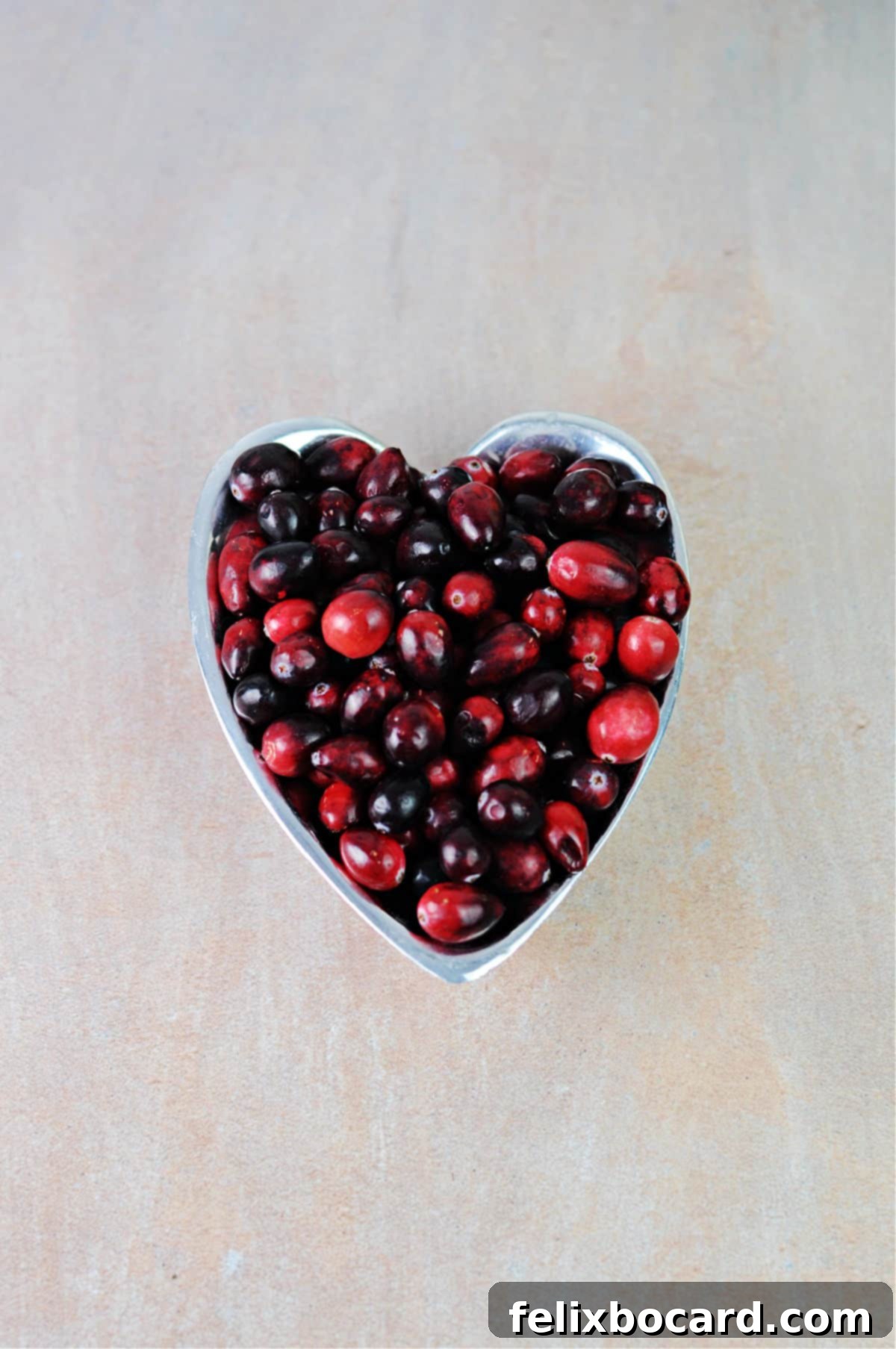 Raw, vibrant red cranberries neatly arranged in a heart-shaped bowl, symbolizing health and natural goodness.