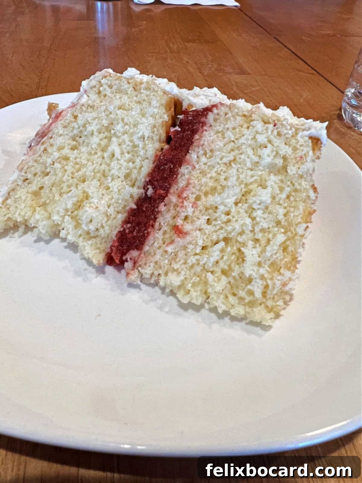 A perfectly cut slice of a two-layer vanilla cake revealing a generous layer of homemade strawberry filling.
