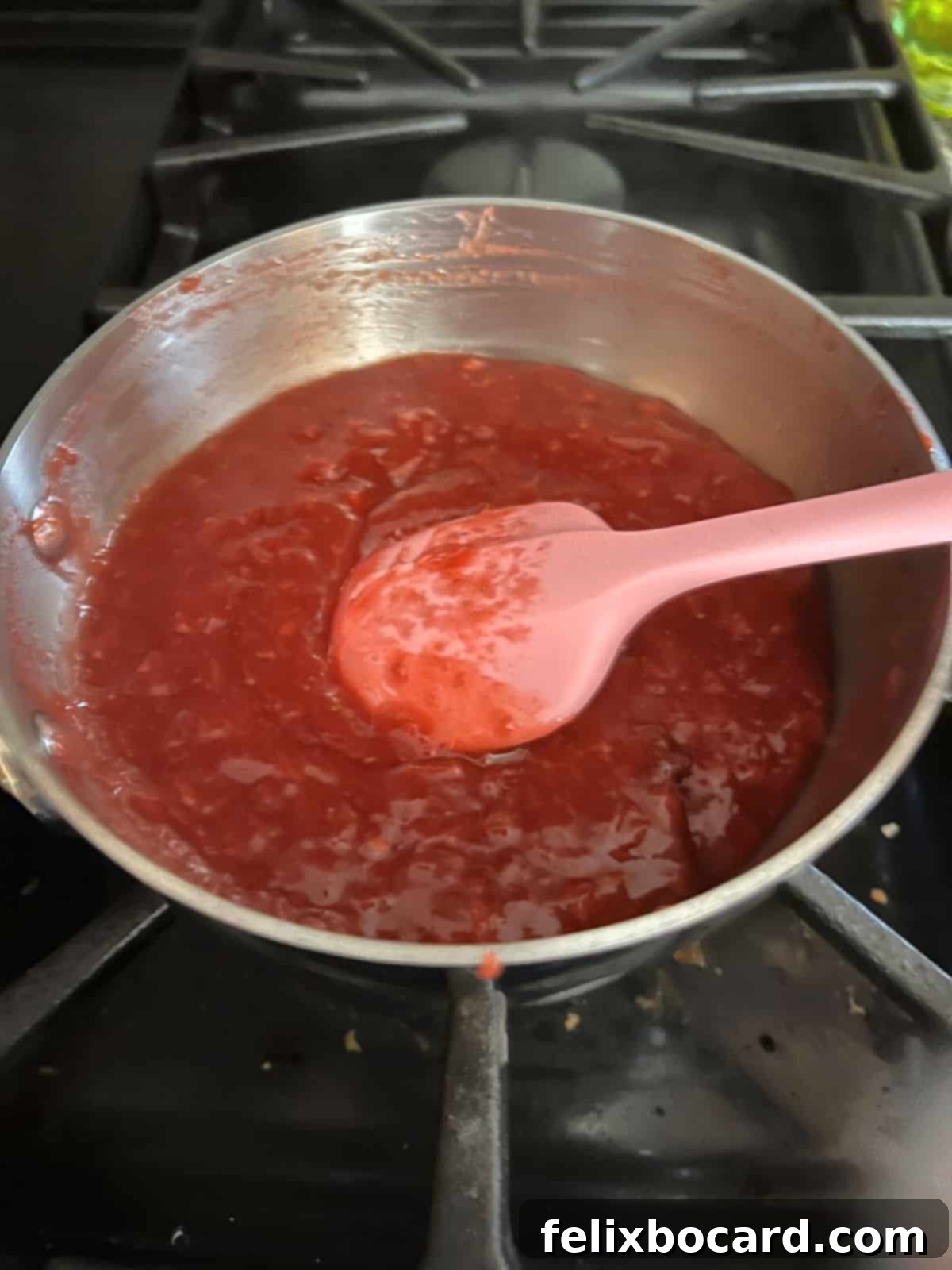 Homemade strawberry filling gently cooking in a saucepan, beginning to thicken beautifully.