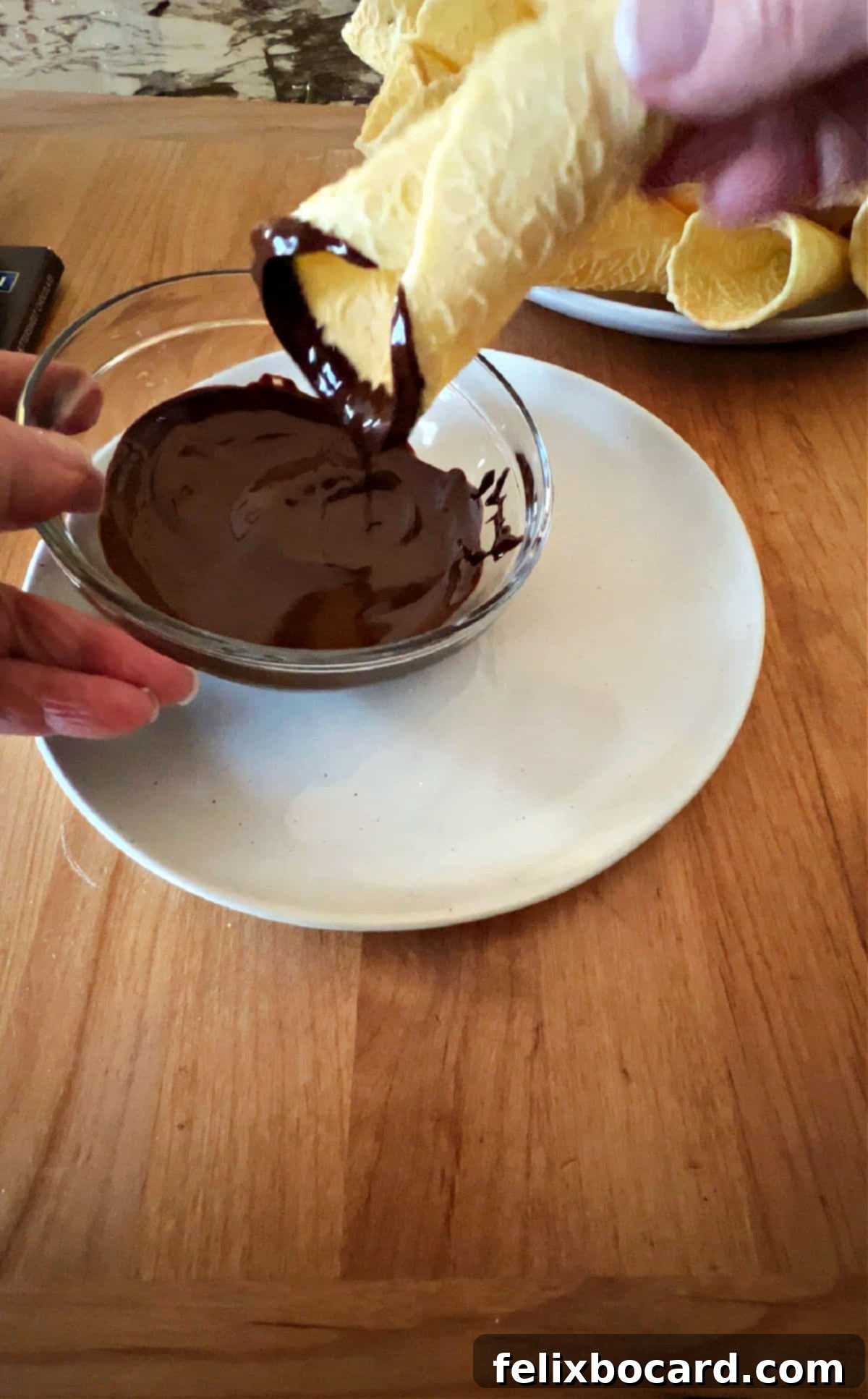 Norwegian Christmas Krumkake 9 A Krumkake cookie being carefully dipped into a bowl of melted chocolate.