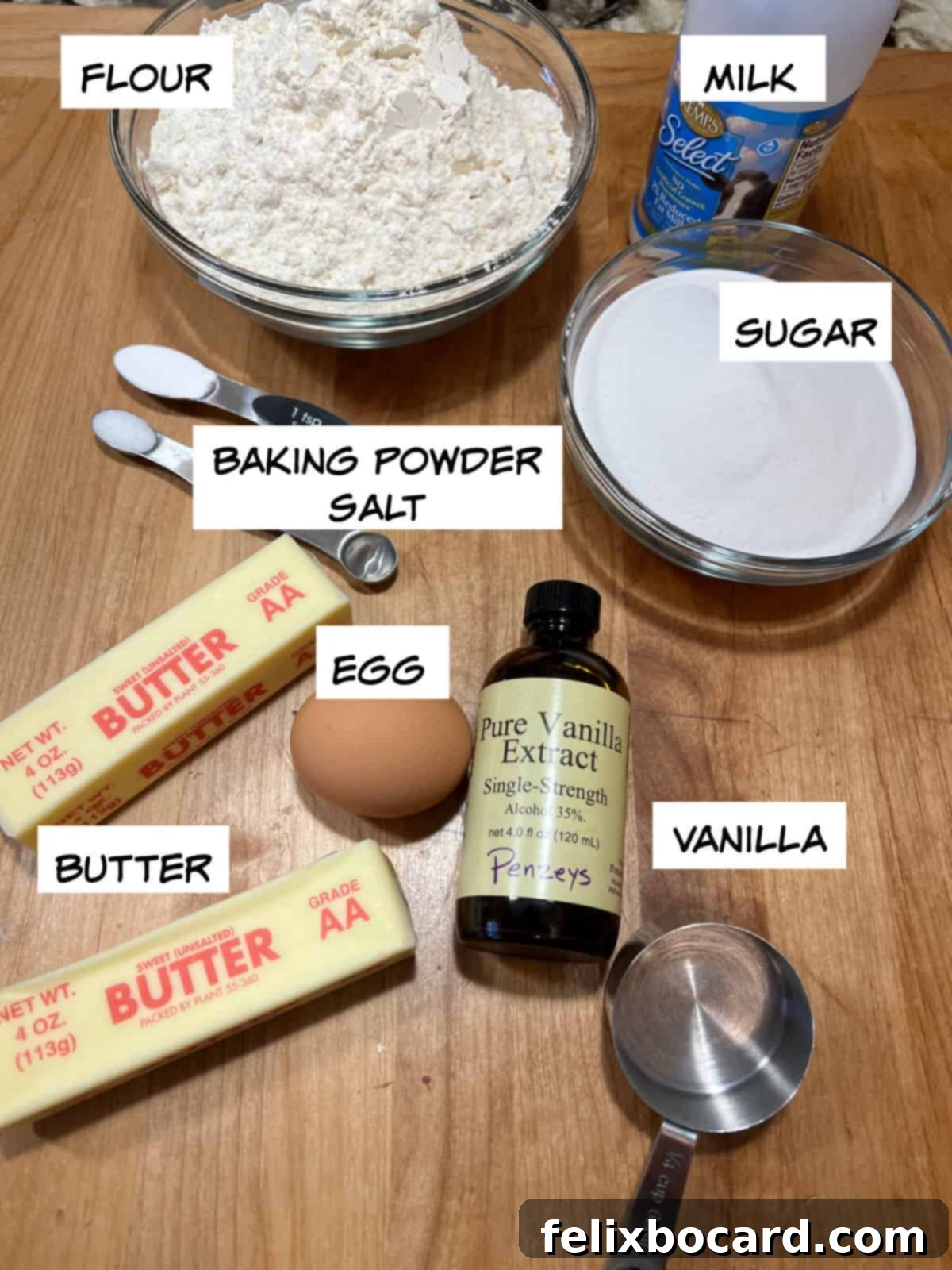 A selection of basic baking ingredients: flour, milk, sugar, baking soda, salt, egg, butter, and vanilla extract.