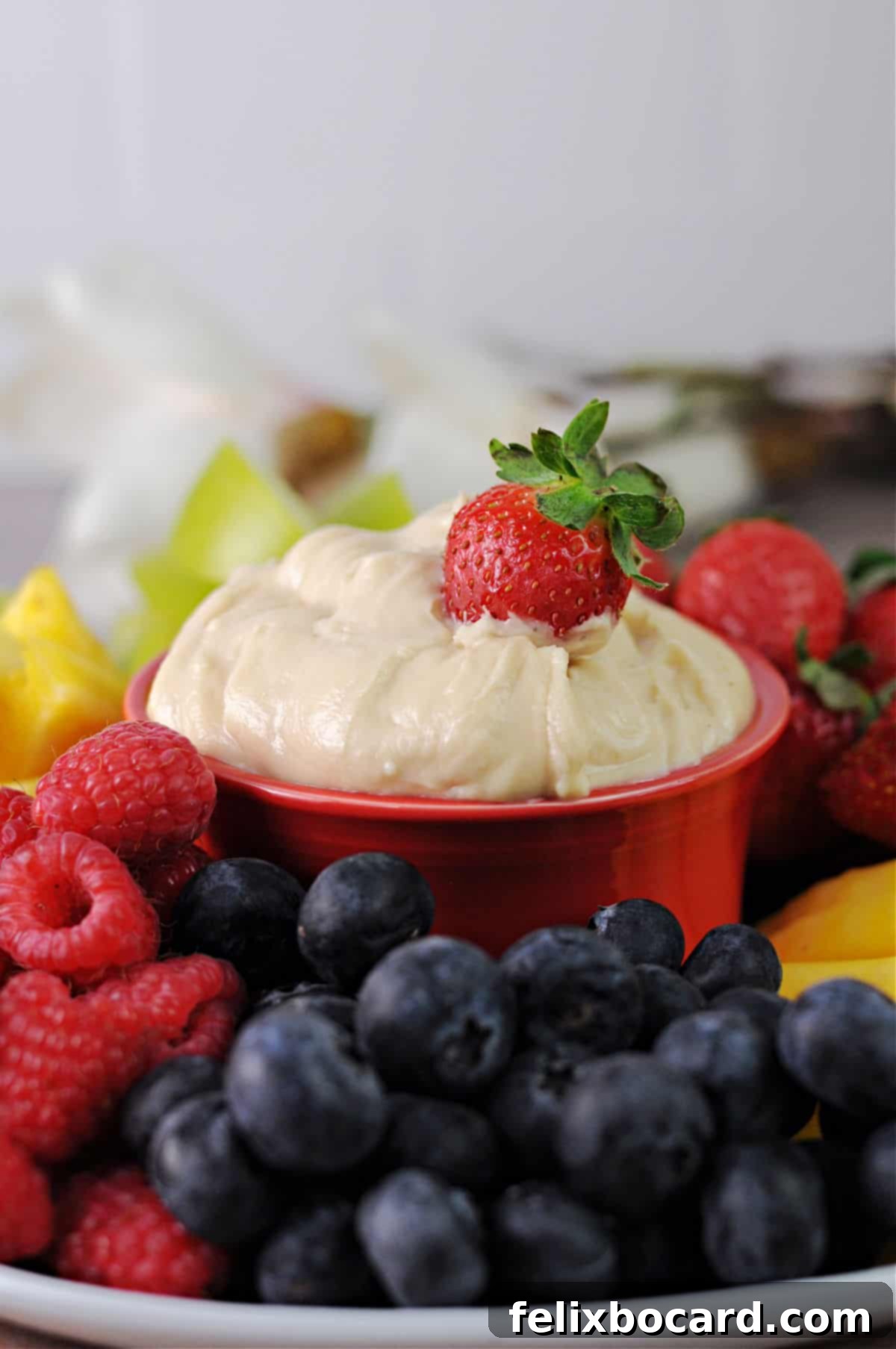Creamy brown sugar cream cheese fruit dip surrounded by a vibrant platter of fresh fruits, including apple slices, grapes, and berries.