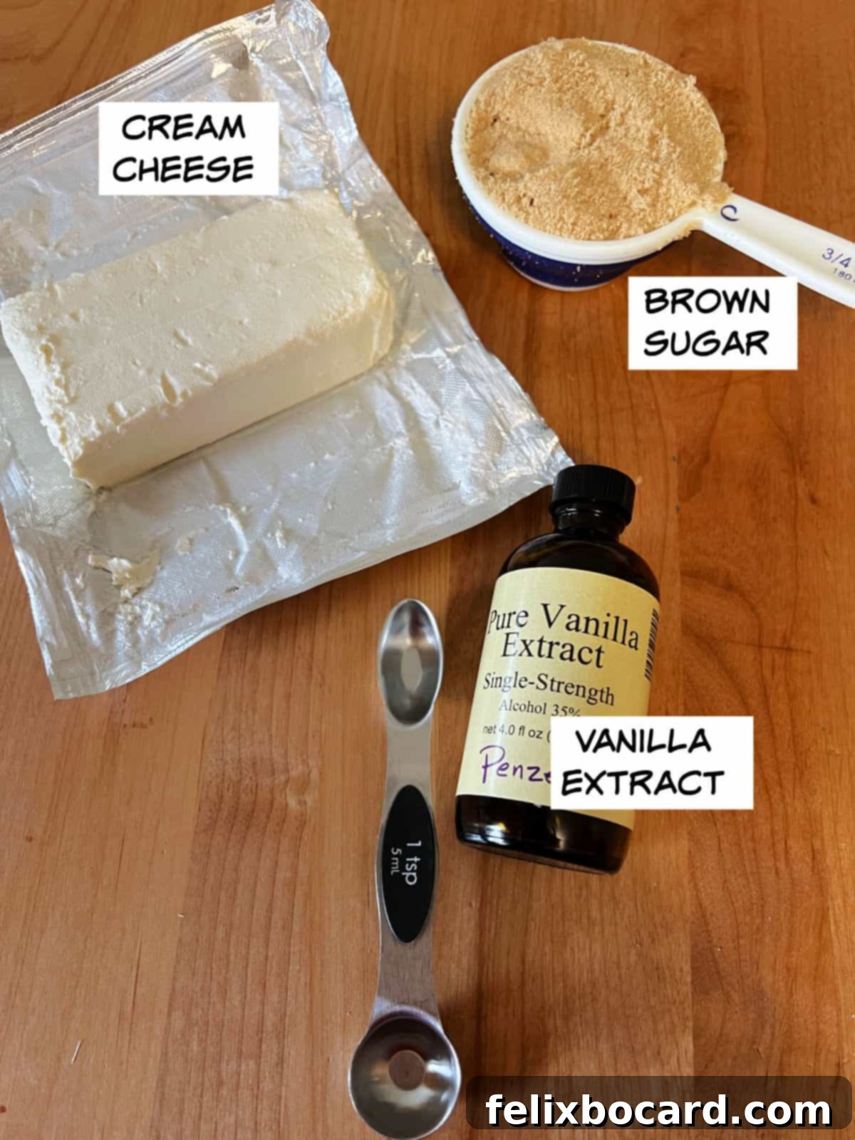 Three essential ingredients for the cream cheese fruit dip: a block of cream cheese, a bowl of brown sugar, and a bottle of vanilla extract.