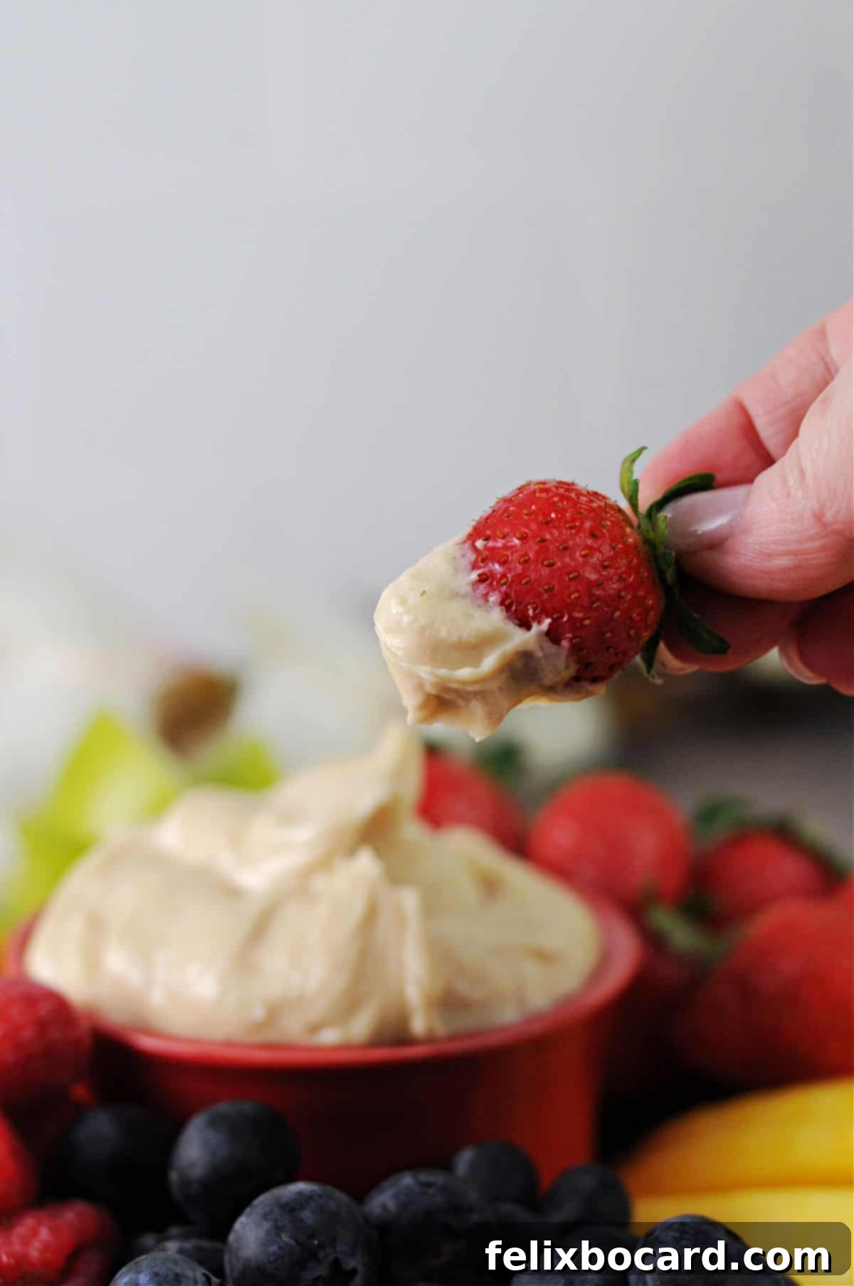 A hand holding a fresh strawberry dipped into the homemade cream cheese and brown sugar fruit dip, ready to be enjoyed.