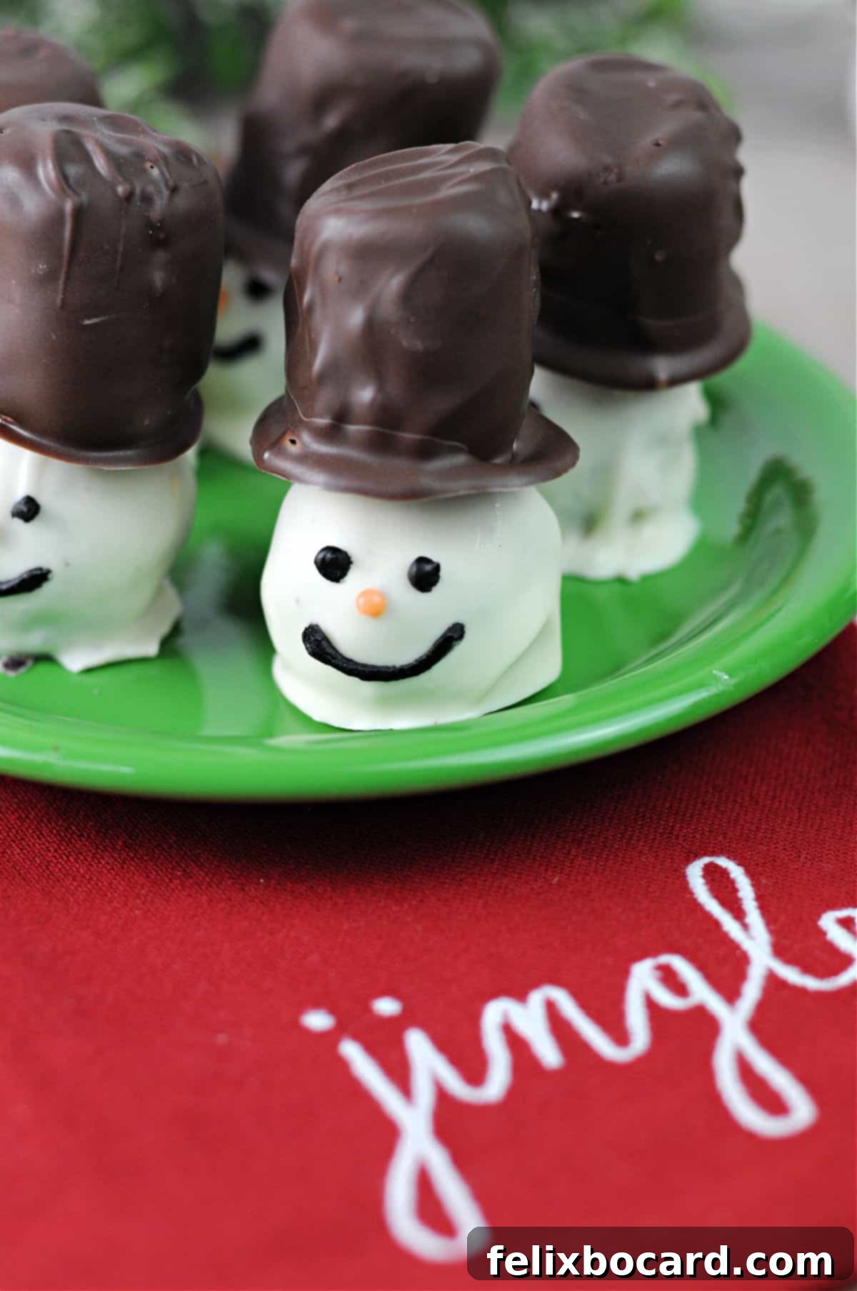 Snowman Oreo Truffles 2 snowman decorated oreo balls on a small green plate resting on a red napkin.