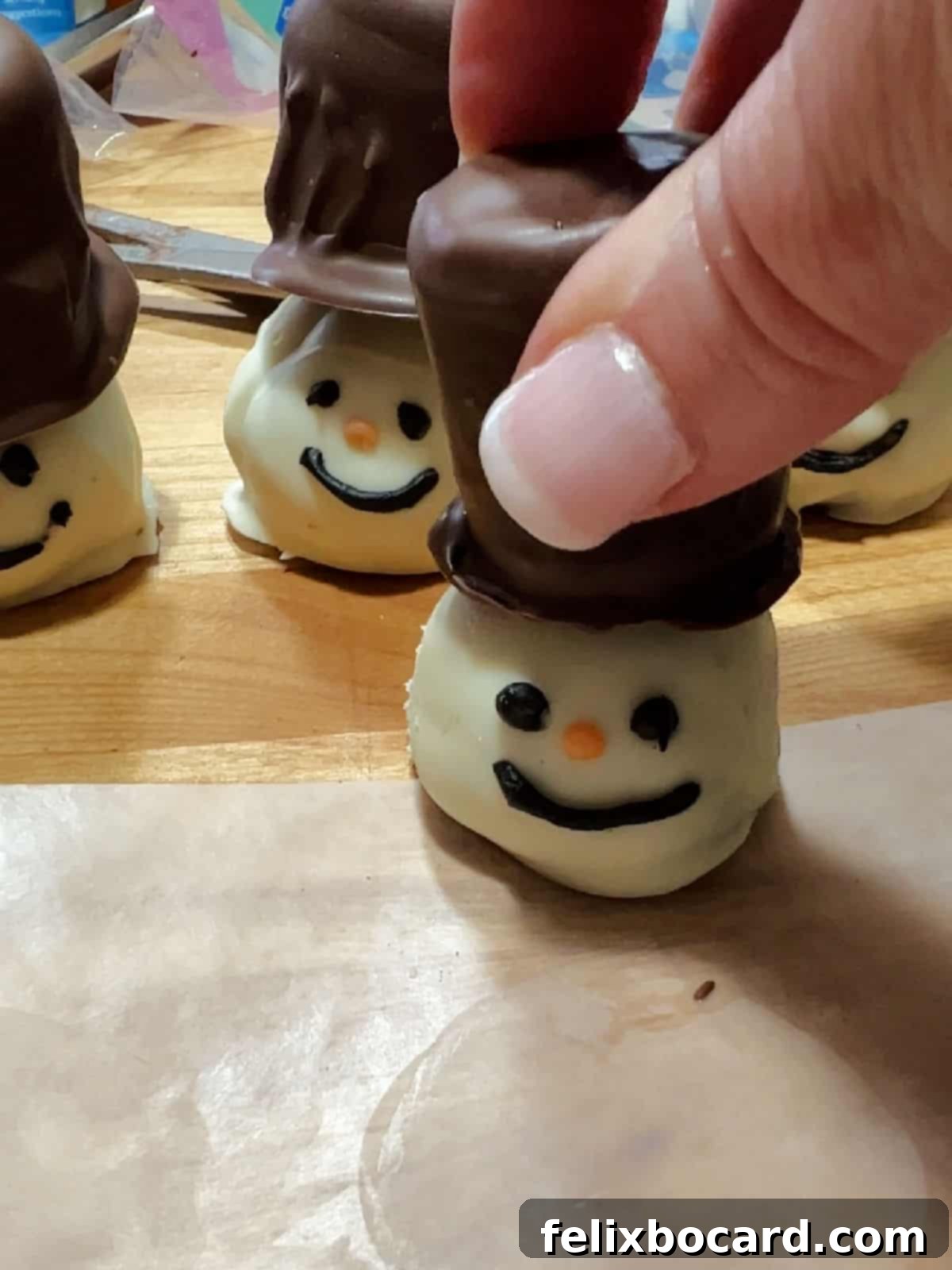 Snowman Oreo Truffles 9 hand placing a hat on top of the oreo ball snowman.
