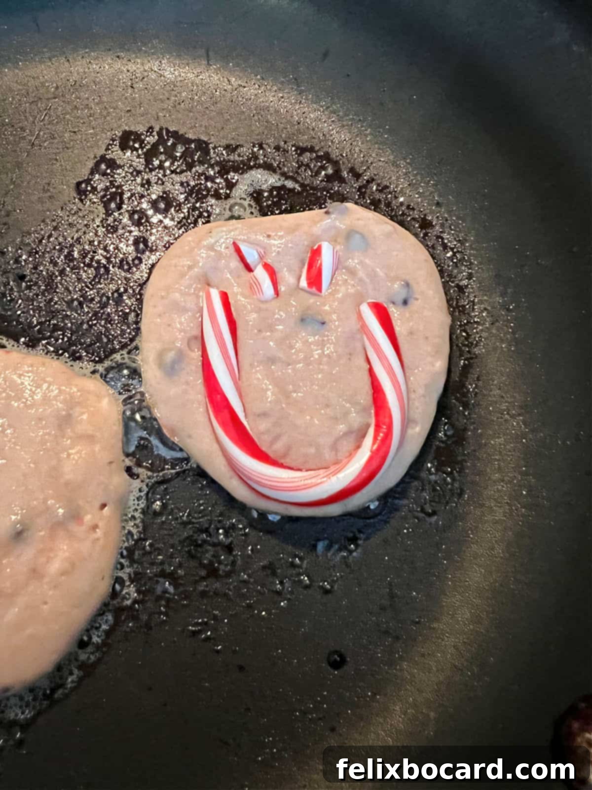 Minty Morning Flapjacks 2 Peppermint pancakes with a cheerful candy cane smiley face cooking in a non-stick pan, steam gently rising.