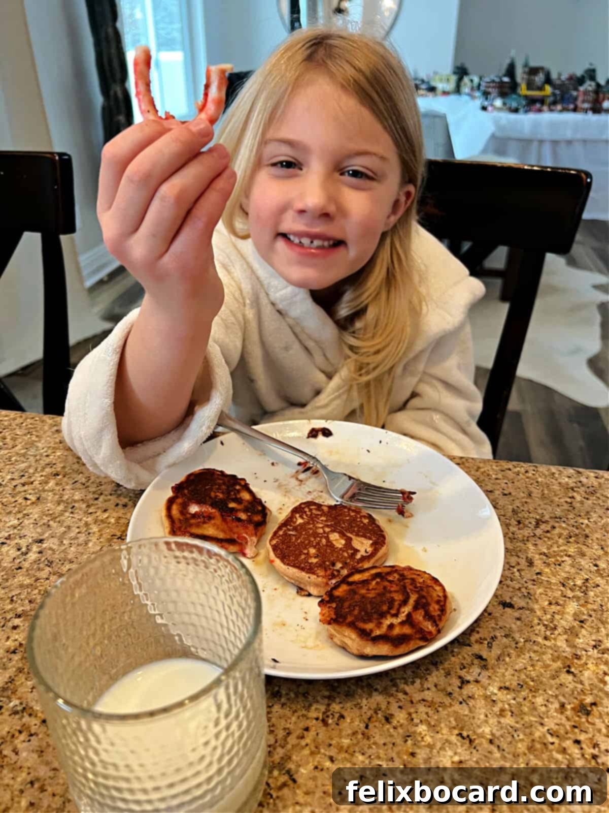 Minty Morning Flapjacks 6 A child's hand holding a candy cane smile, carefully pulled from a cooked peppermint pancake, against a blurred background.