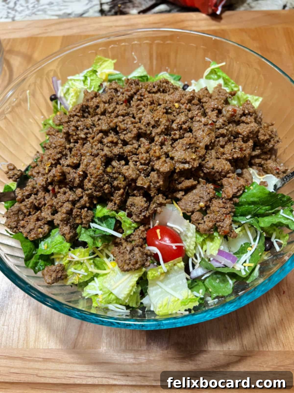 Seasoned taco meat being added to a large bowl of fresh salad ingredients, prior to mixing with dressing.