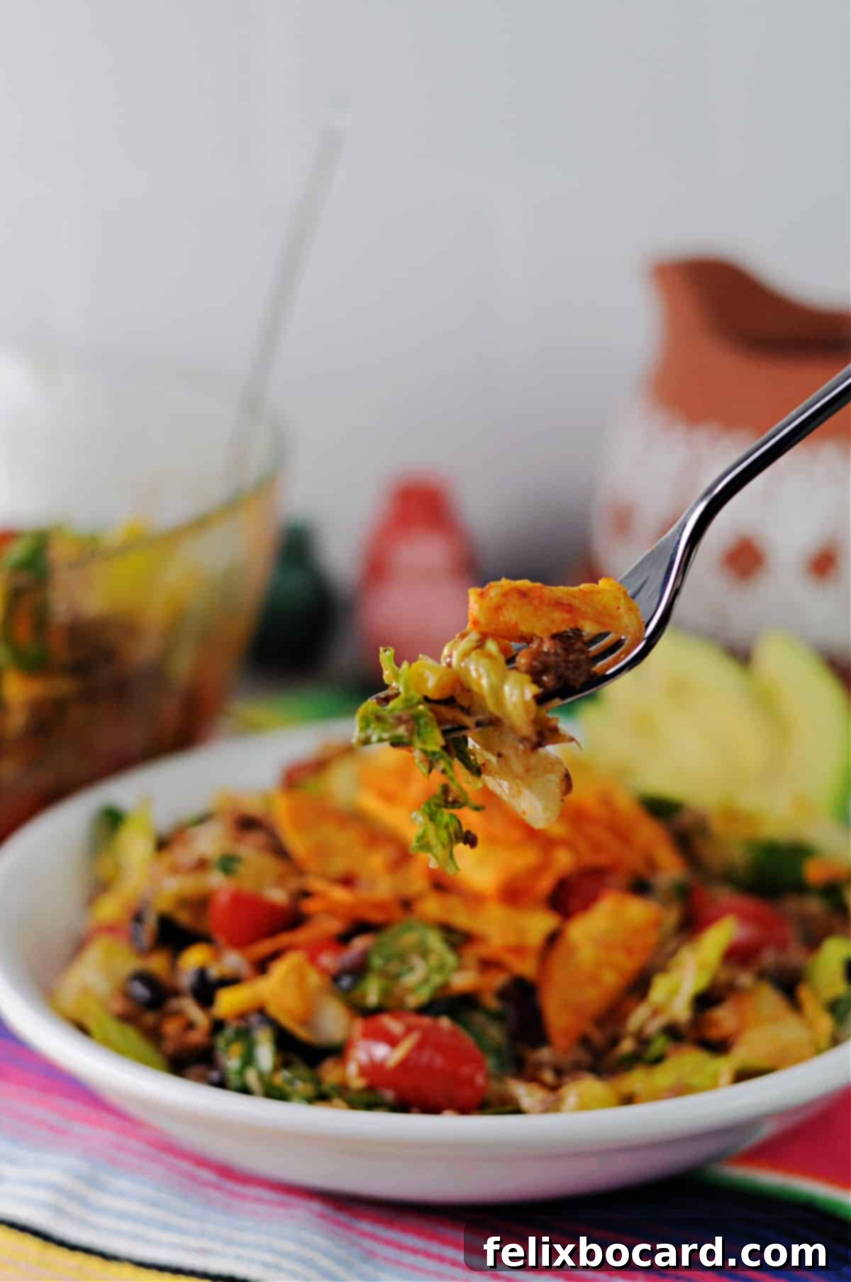 A forkful of vibrant Dorito taco salad, showcasing the crispy chips, seasoned meat, and fresh vegetables, ready to be eaten.