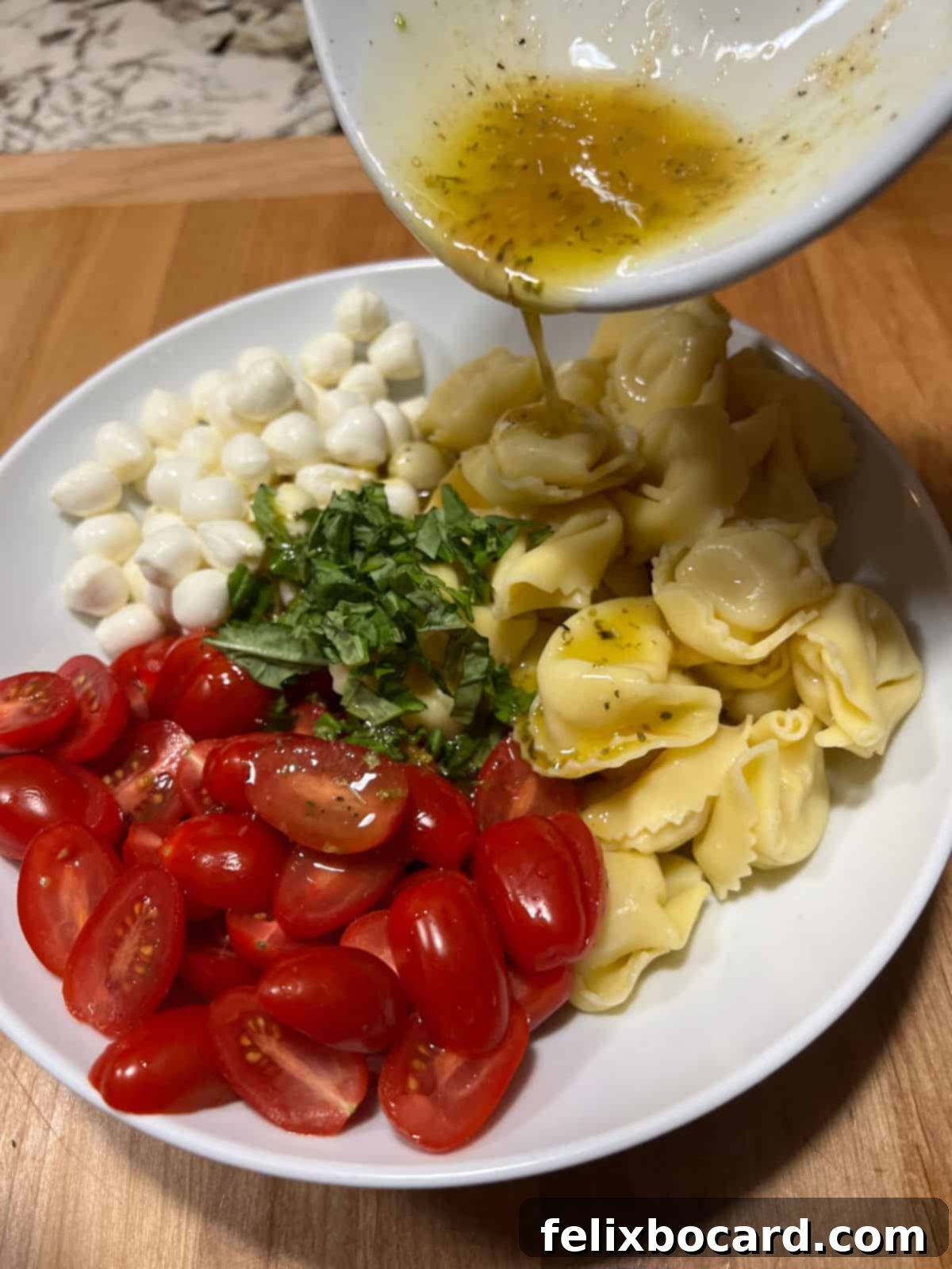 Vibrant Caprese Tortellini Salad 5 A bowl of Caprese tortellini salad ingredients being tossed with the homemade dressing, ensuring every piece is coated.