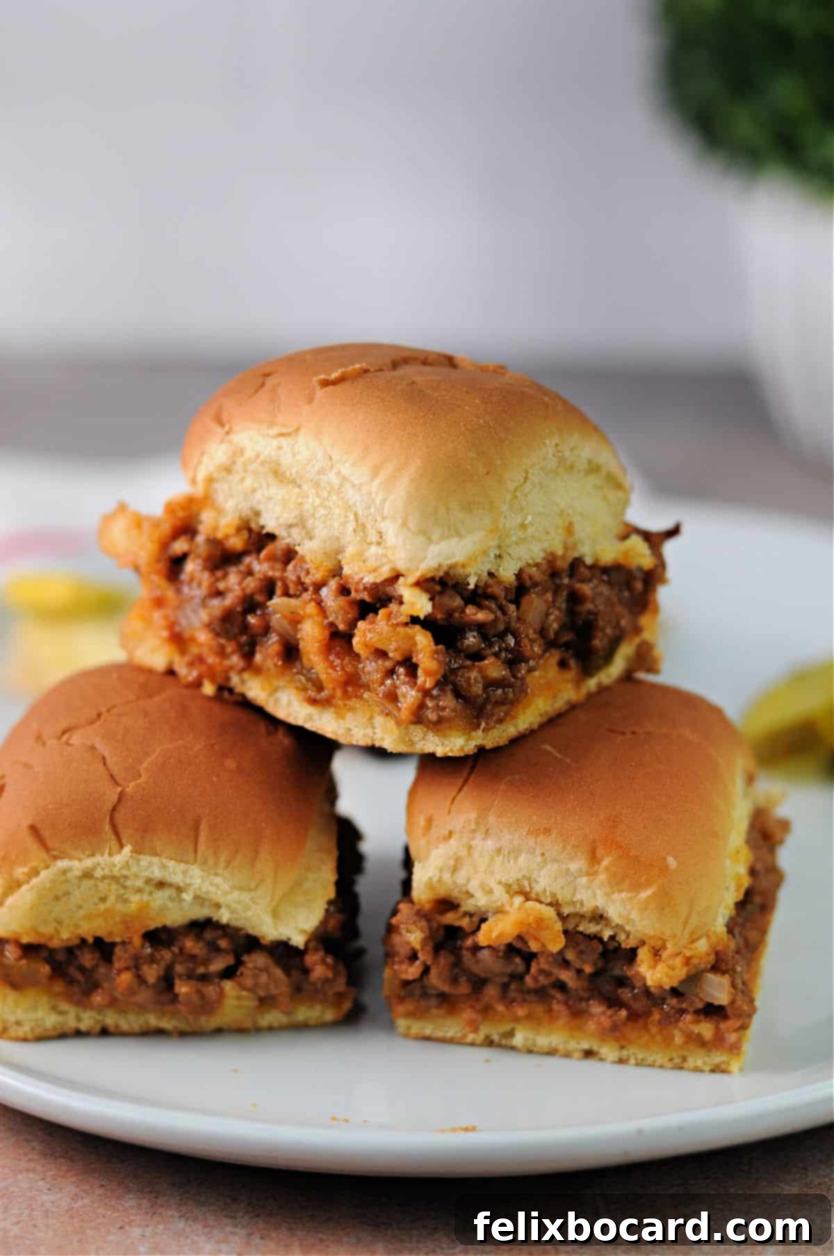 Three perfectly baked sloppy joe sliders arranged on a serving plate, showcasing their crispy edges and rich filling.