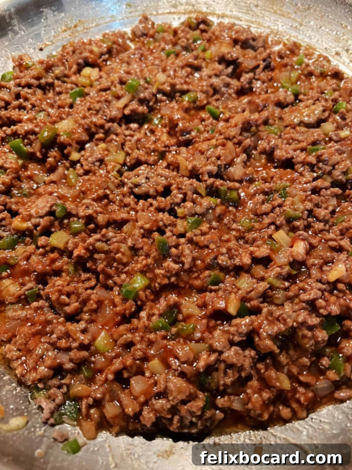 Ground beef and vegetables simmering in a rich, red sloppy joe sauce within a cast iron skillet.
