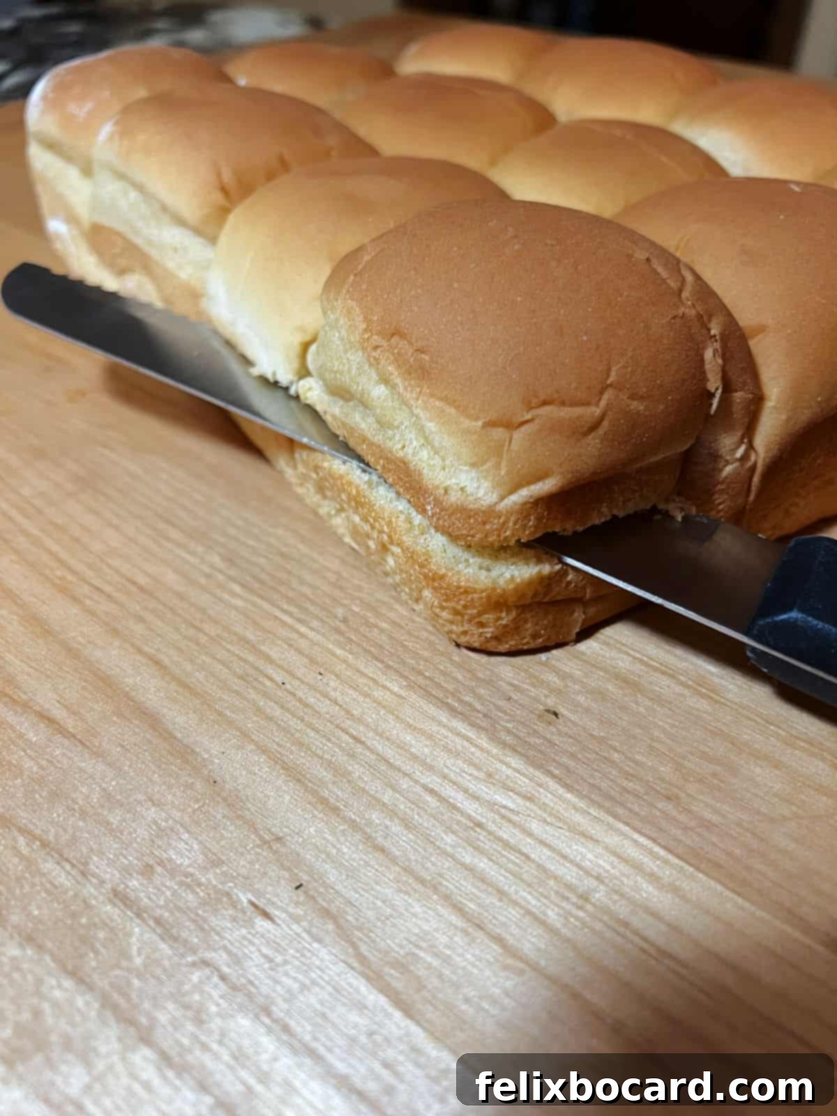 A serrated knife slicing horizontally through a connected block of dinner rolls to create top and bottom halves.