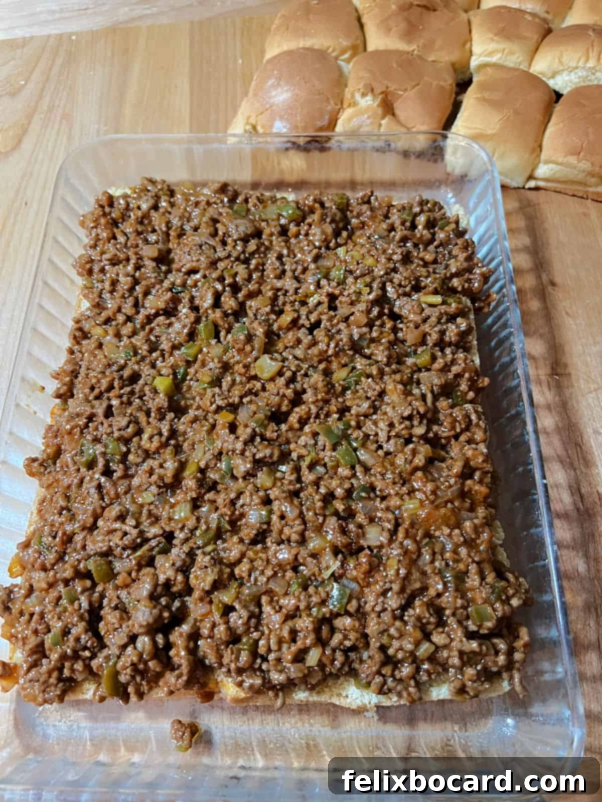 A baking dish with the bottom layer of dinner rolls covered generously with the sloppy joe meat mixture.