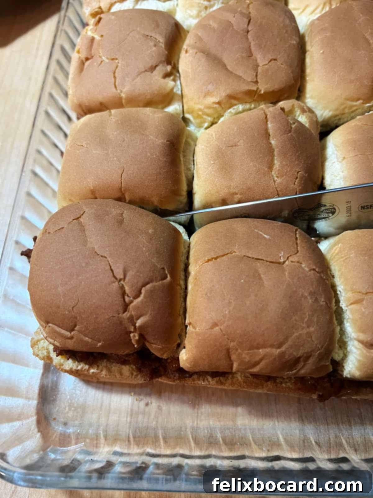 A sharp knife carefully cutting individual sloppy joe sliders from the baked block in a pan.