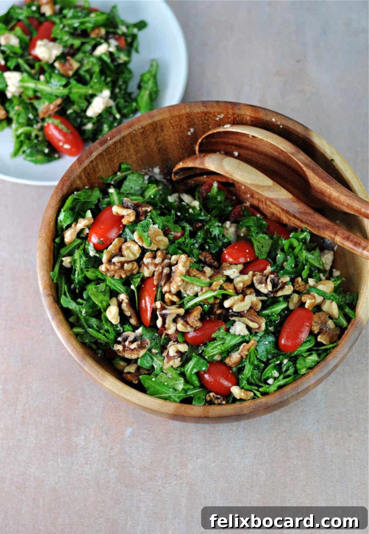 A beautiful wood serving bowl filled with a fresh Arugula Feta Tomato Salad, ready for guests.