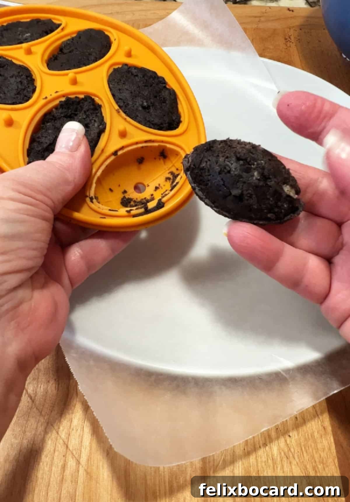 A hand gently removing a perfectly formed football-shaped Oreo truffle from a silicone mold.