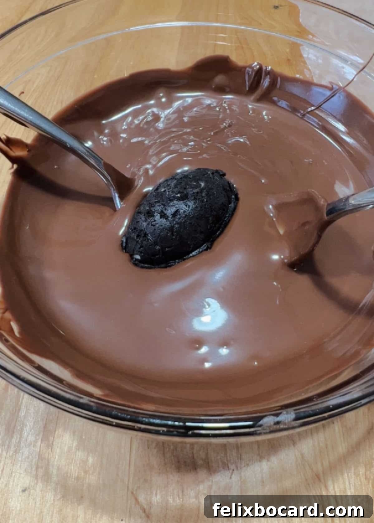 An Oreo football truffle carefully dipped into a bowl of melted chocolate candy coating, ready to be fully submerged.
