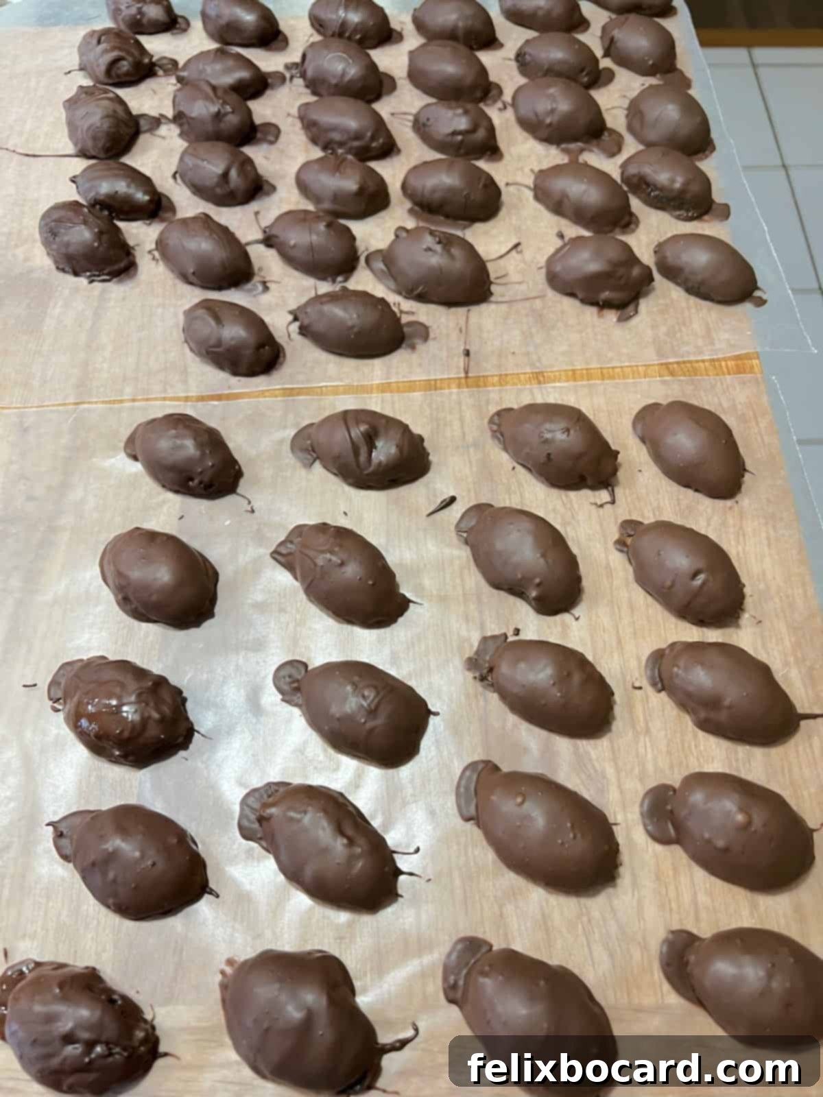 Several chocolate-coated football Oreo truffles drying on a sheet of wax paper, awaiting decoration.