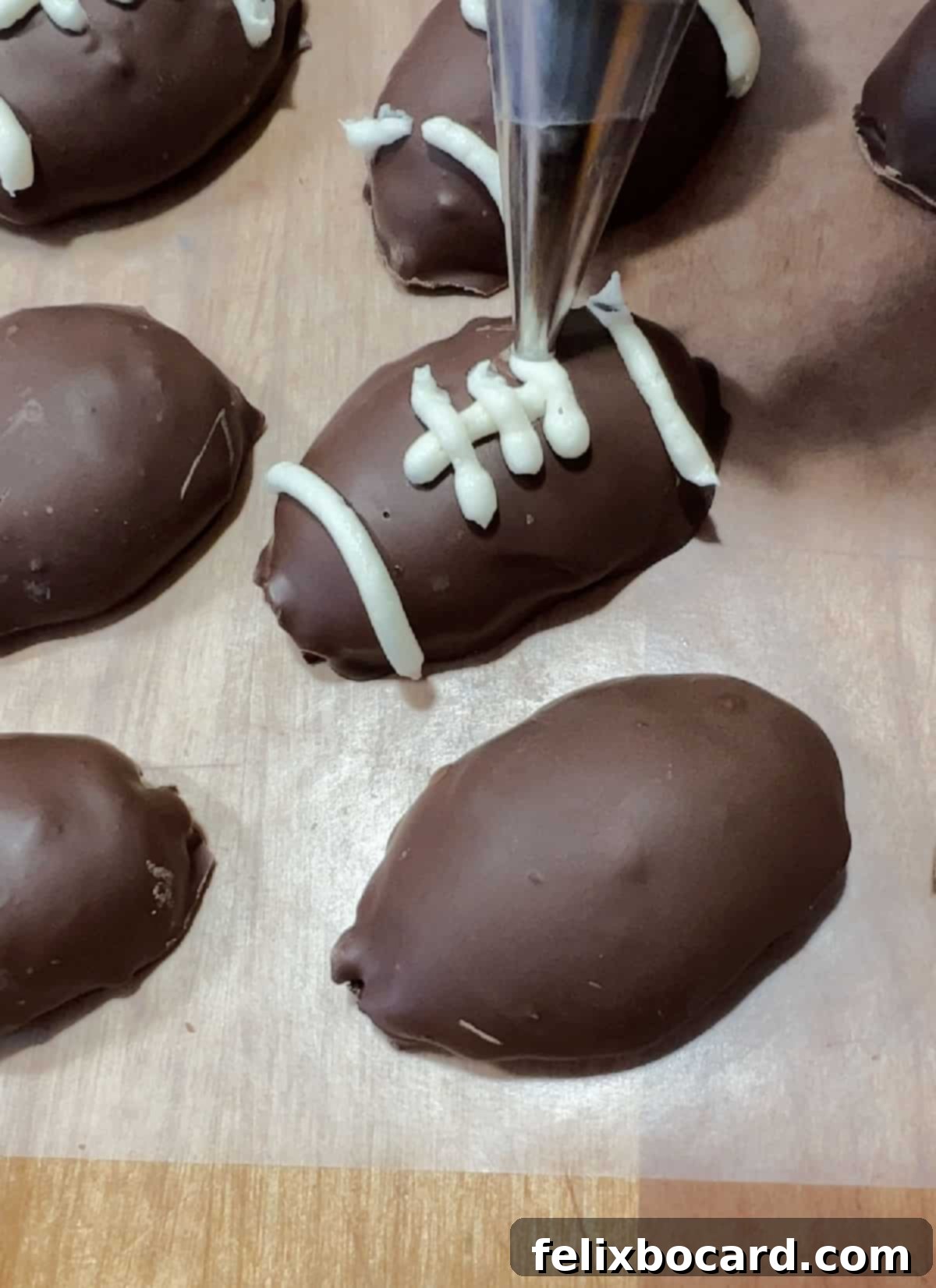 Decorating an Oreo football truffle by piping white frosting onto it to create the distinct markings and laces of a football.