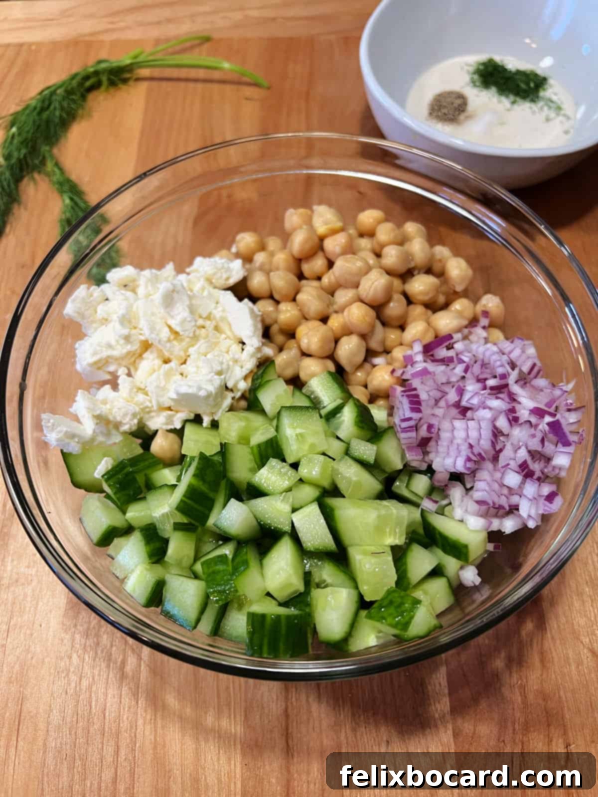 Prepared salad ingredients in a bowl: chickpeas, cucumber, red onion, and feta.