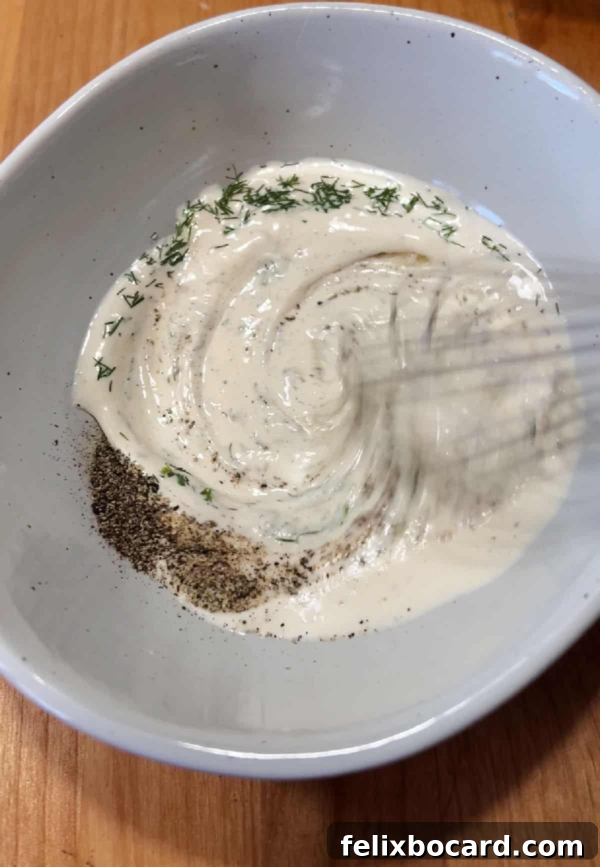 Hand mixing ranch dressing with fresh dill, salt, and pepper in a small bowl.