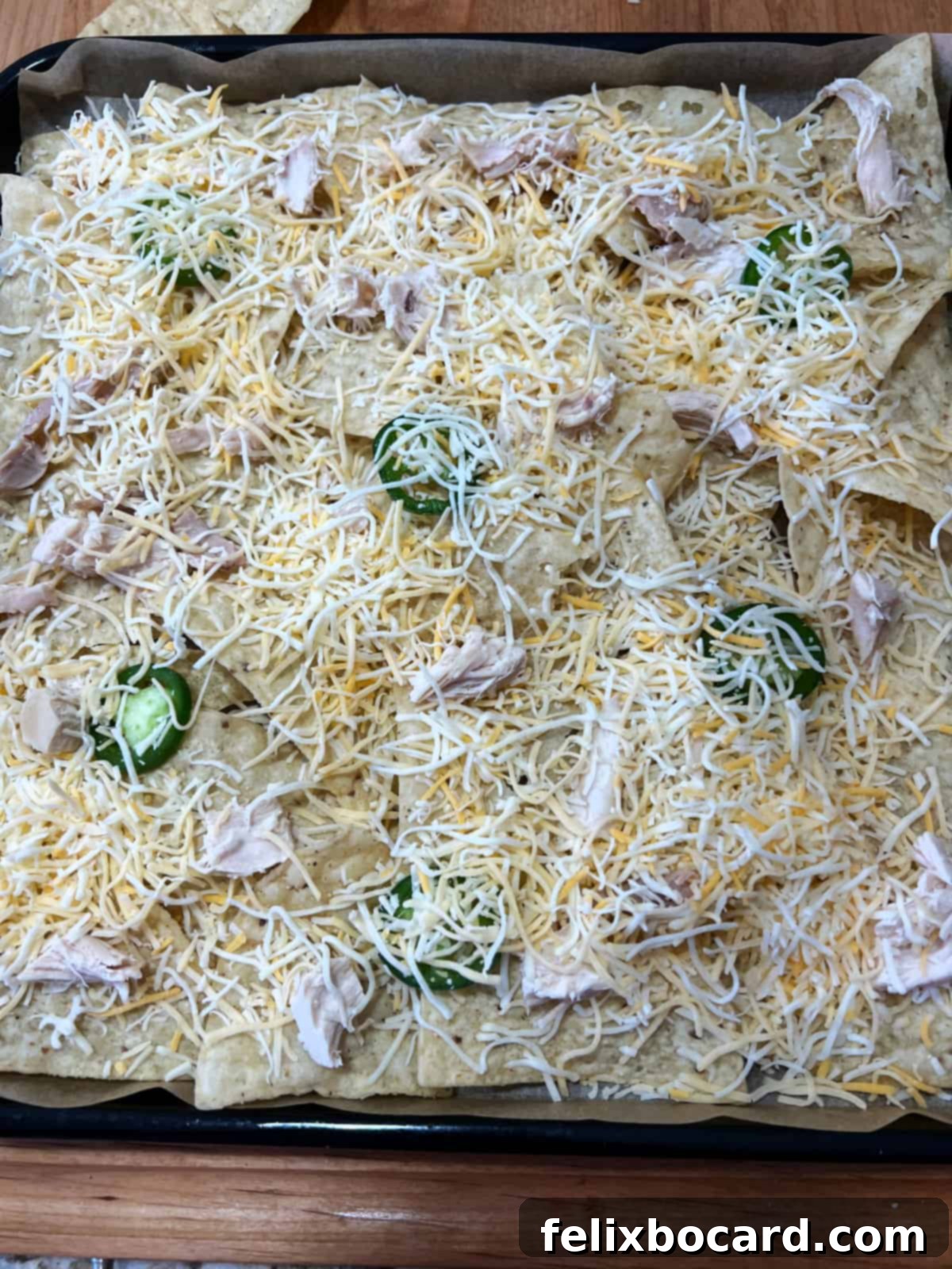 A close-up view of the first layer of nachos on an air fryer tray, showing tortilla chips covered with shredded chicken, cheese, and jalapeno slices.