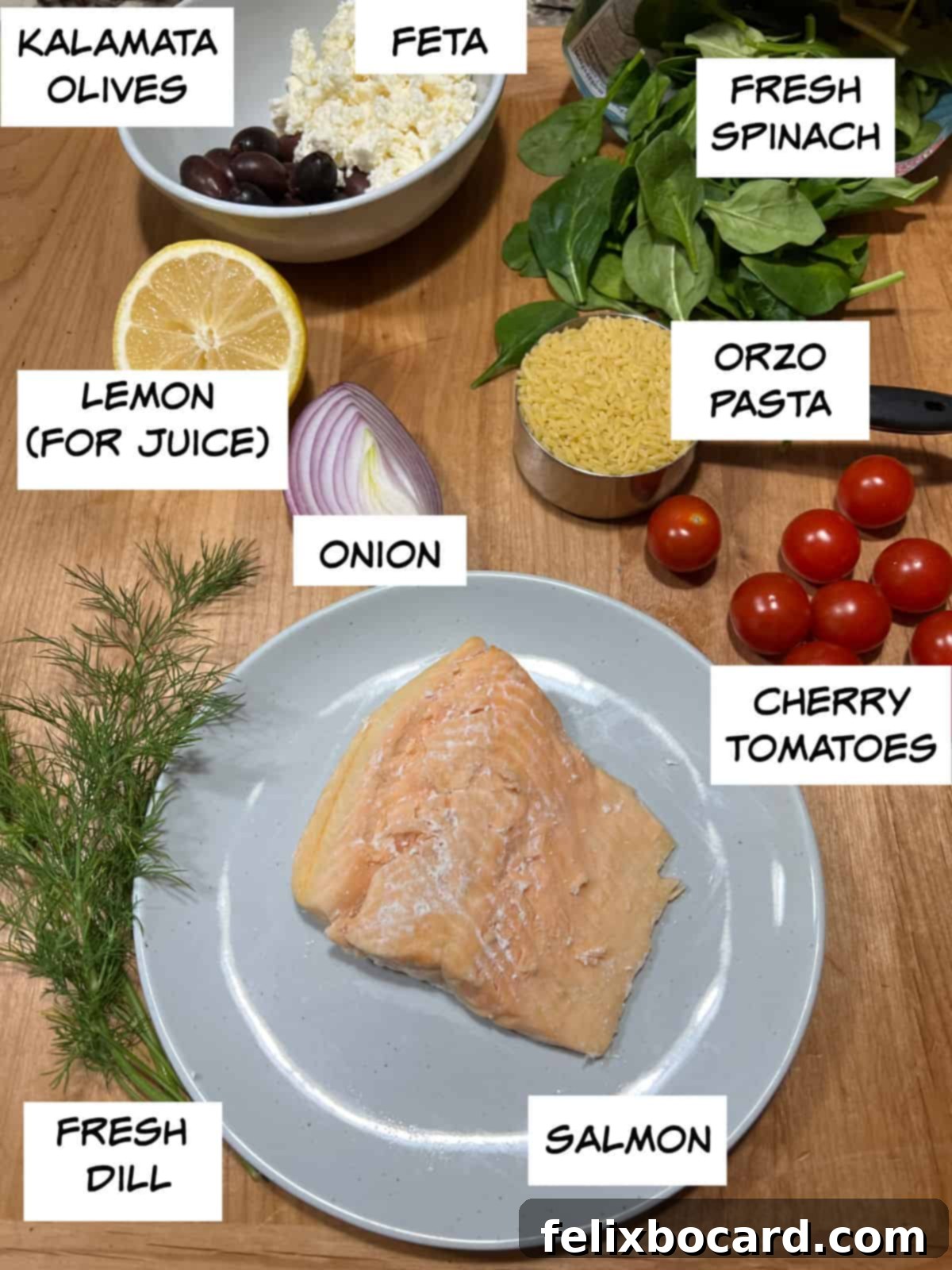 A flat lay photograph showcasing all the fresh ingredients for Salmon Orzo Salad: salmon fillet, cherry tomatoes, orzo pasta, fresh spinach, crumbled feta cheese, Kalamata olives, lemon, red onion, and fresh dill.