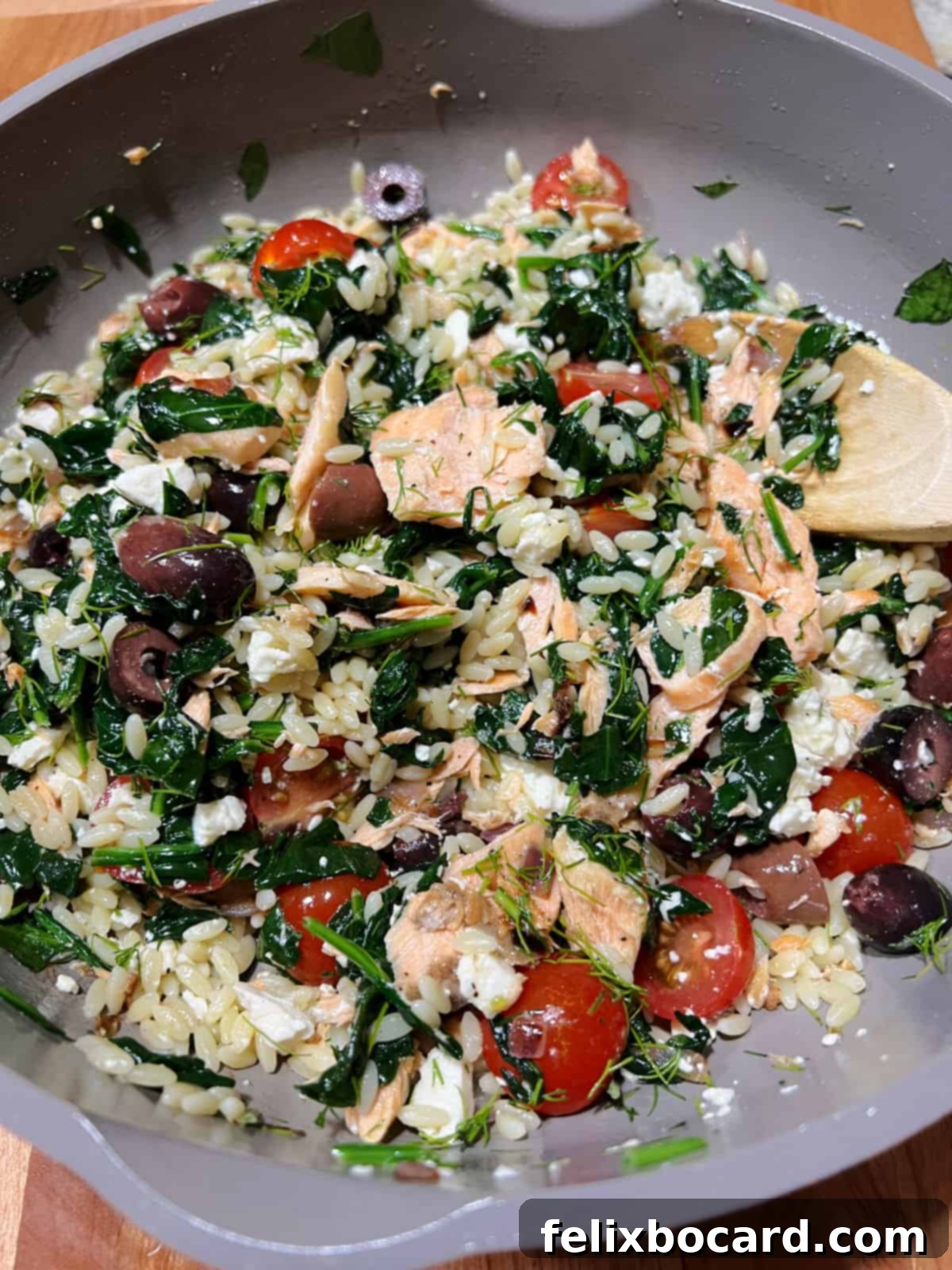A completed Salmon Orzo Salad, vibrant with colors, mixed thoroughly in a skillet and ready to be served.