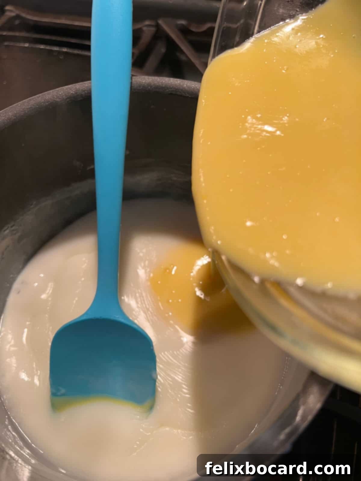 Tempered egg mixture being slowly added back to the saucepan with the hot pudding base.