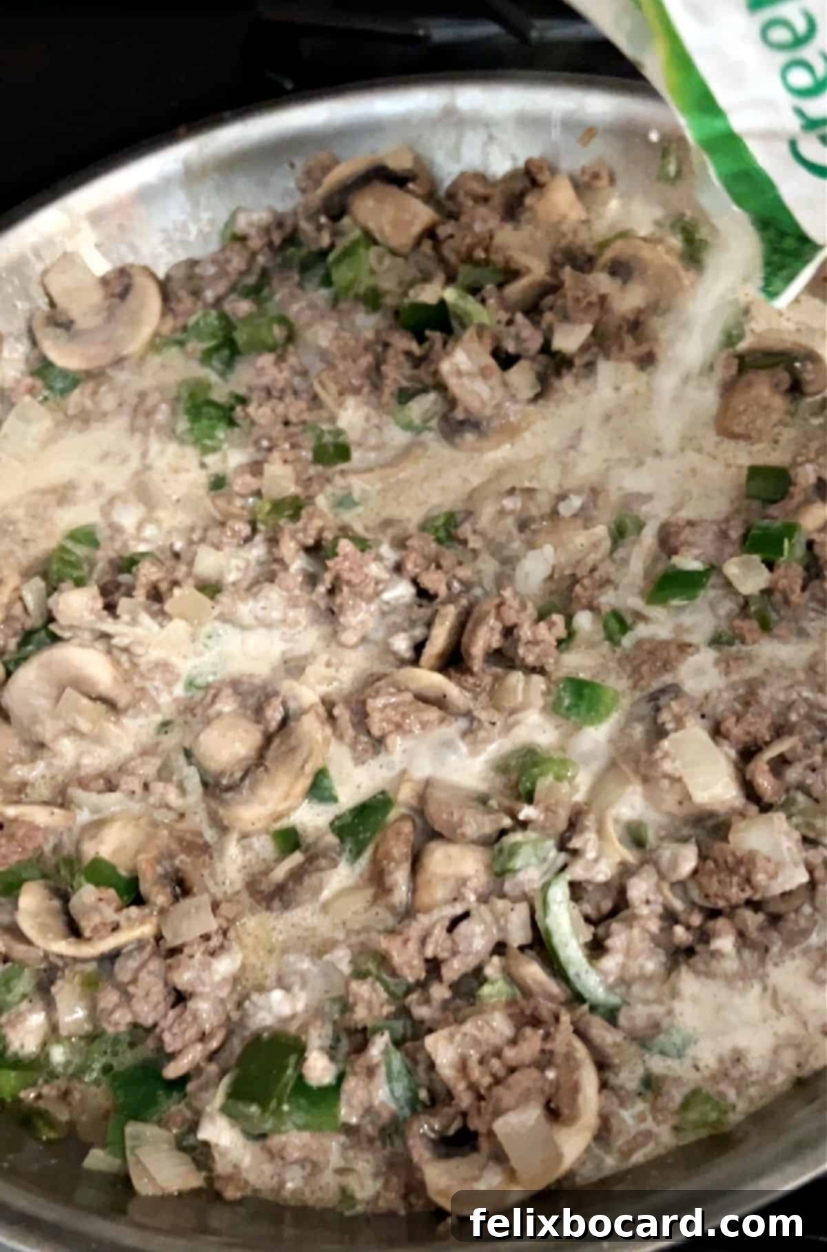 Cooked riced cauliflower being added to the savory ground beef and vegetable mixture in a skillet, blending into the creamy sauce.