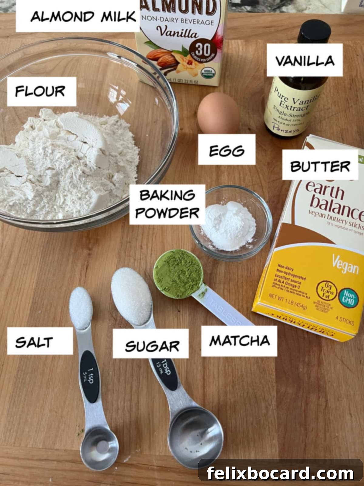 Fluffy Matcha Pancakes 3 A flat lay photograph showcasing all the ingredients required for matcha pancakes: almond milk, vanilla extract, an egg, melted butter, all-purpose flour, baking powder, granulated sugar, salt, and vibrant green matcha powder.