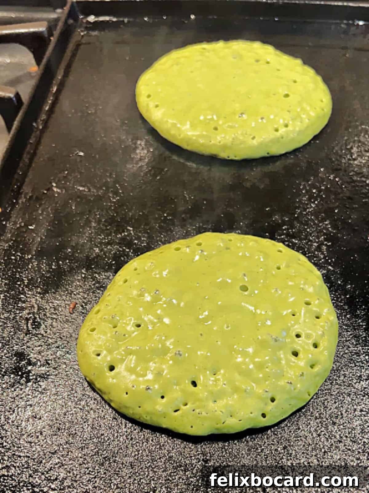 Fluffy Matcha Pancakes 6 Several vibrant green matcha pancakes cooking on a hot cast iron griddle, with bubbles forming on their surface.