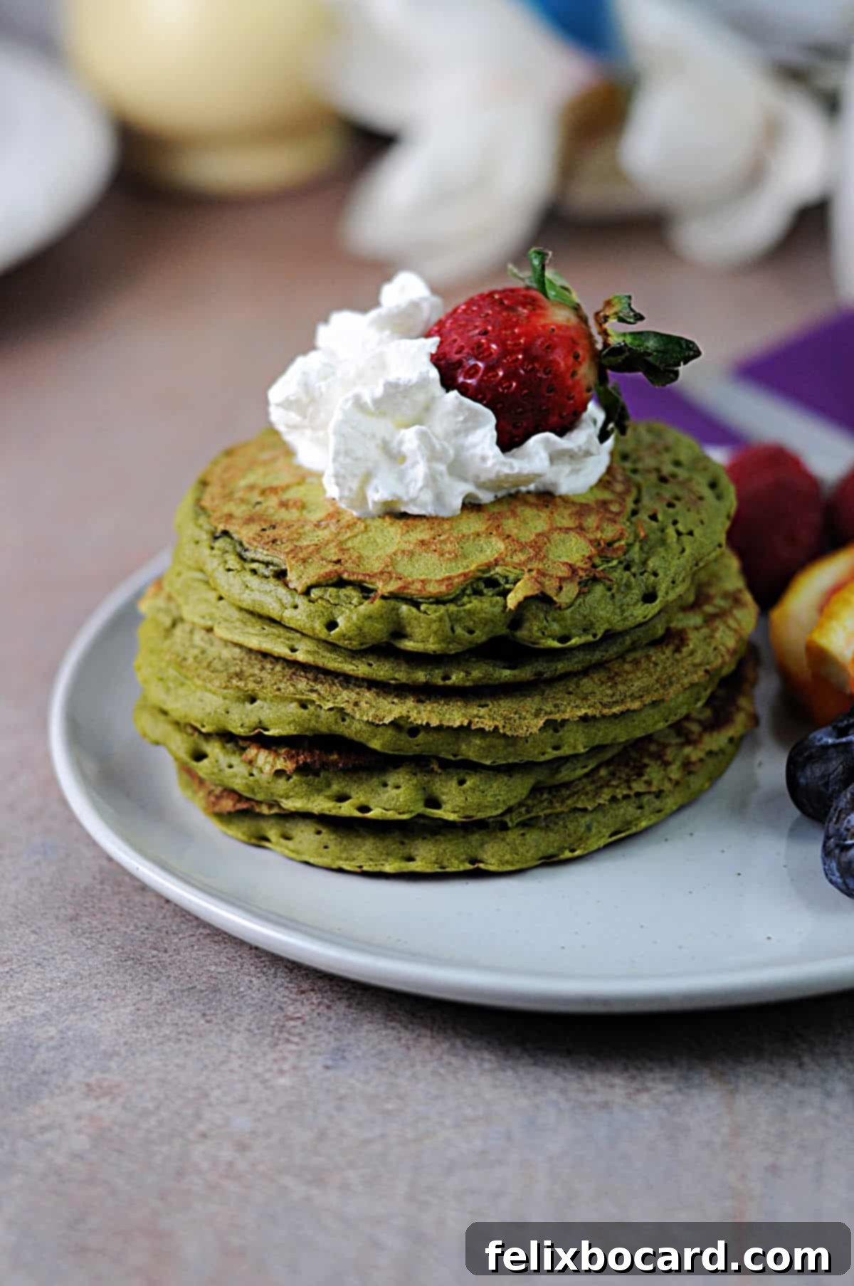 Fluffy Matcha Pancakes 7 A tall, inviting stack of vibrant green matcha pancakes, elegantly garnished with a dollop of whipped cream and a fresh strawberry on top.
