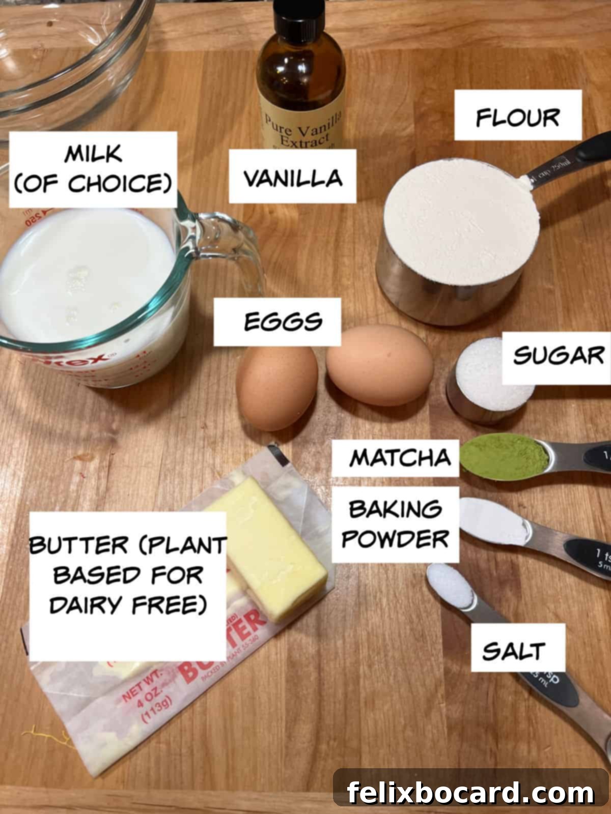 A beautifully arranged selection of ingredients: milk, vanilla extract, all-purpose flour, eggs, granulated sugar, matcha powder, baking powder, salt, and melted butter.
