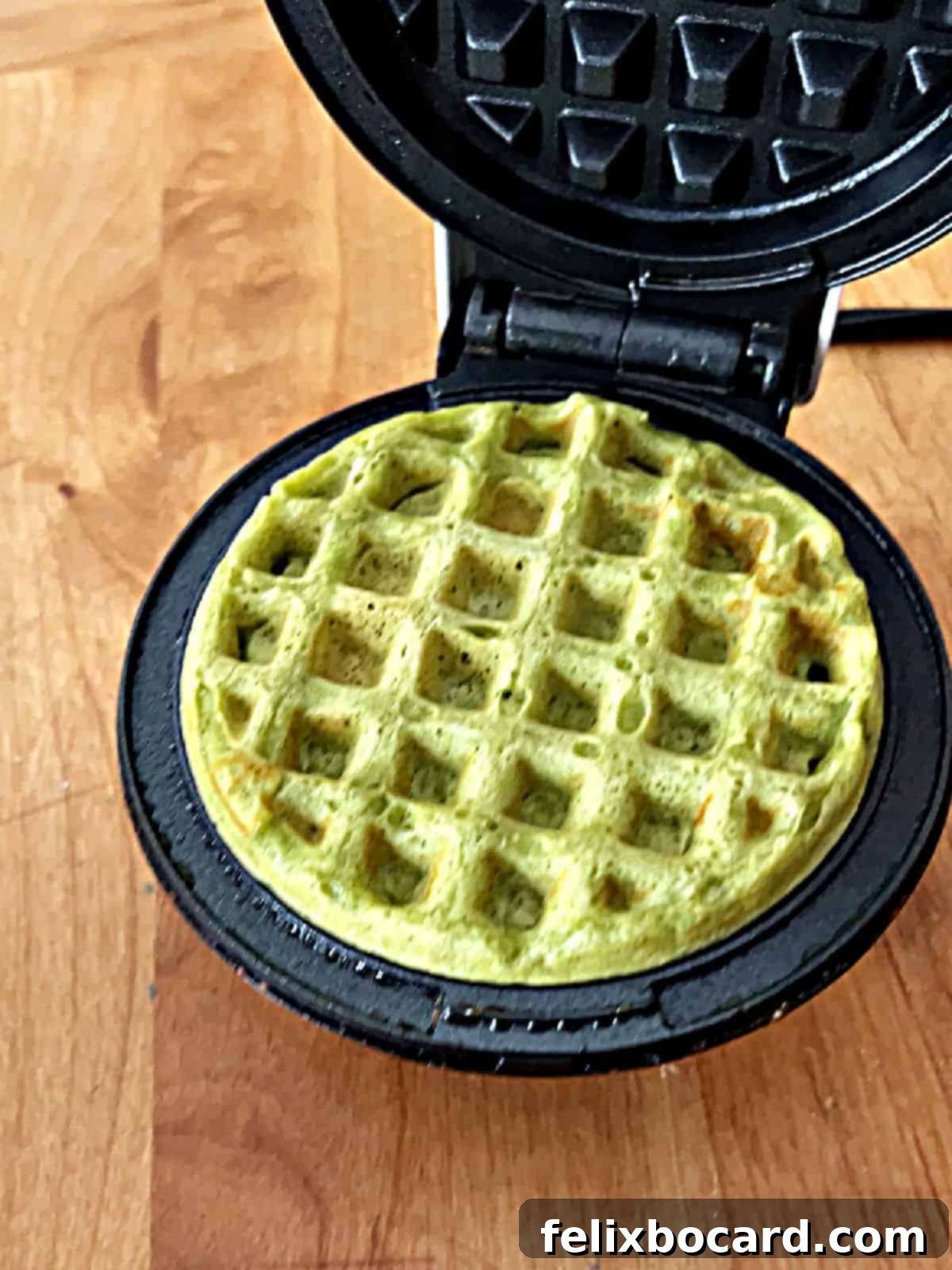 A mini matcha waffle cooking inside a Dash mini waffle iron, highlighting its vibrant green color.