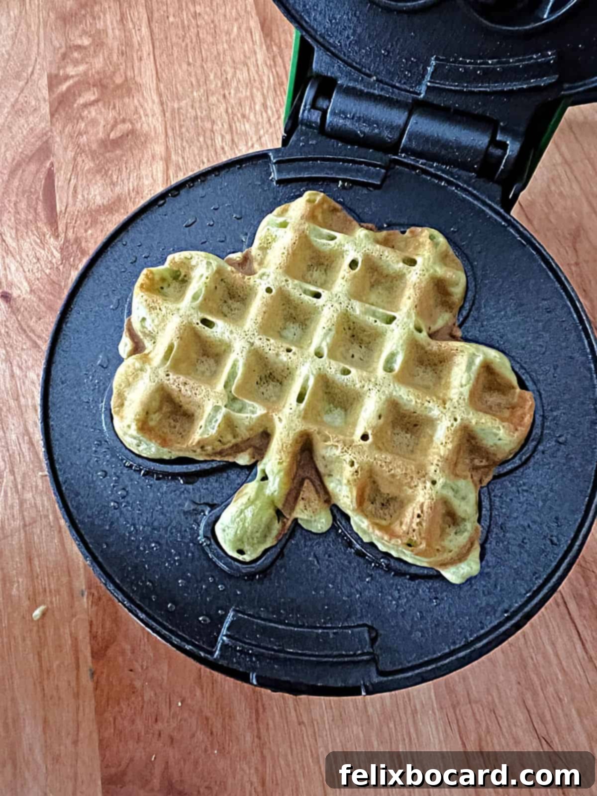 A festive shamrock-shaped mini matcha waffle cooking in a special waffle iron, ideal for St. Patrick's Day.