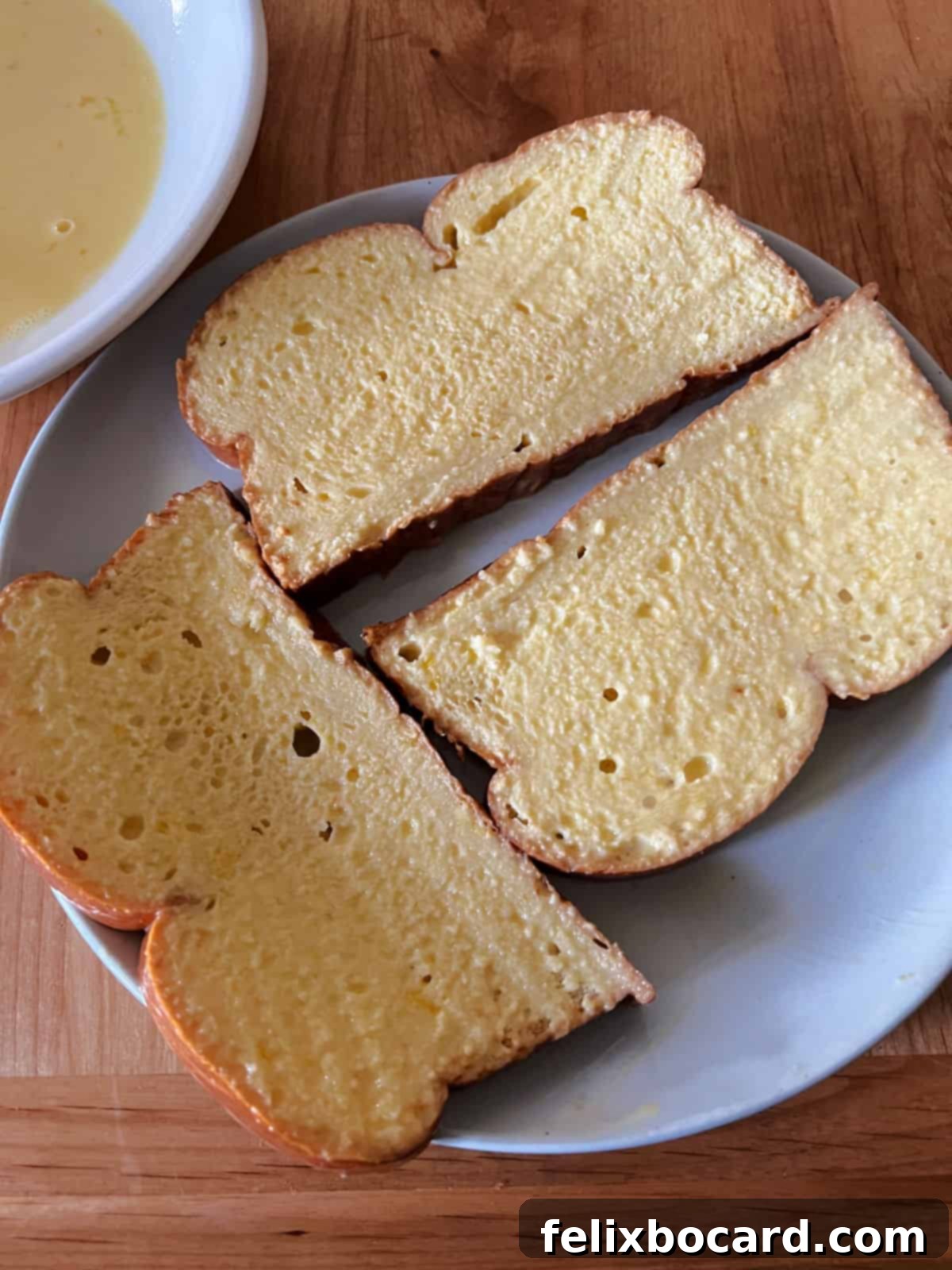 Slices of bread evenly coated in egg mixture, resting on a plate.